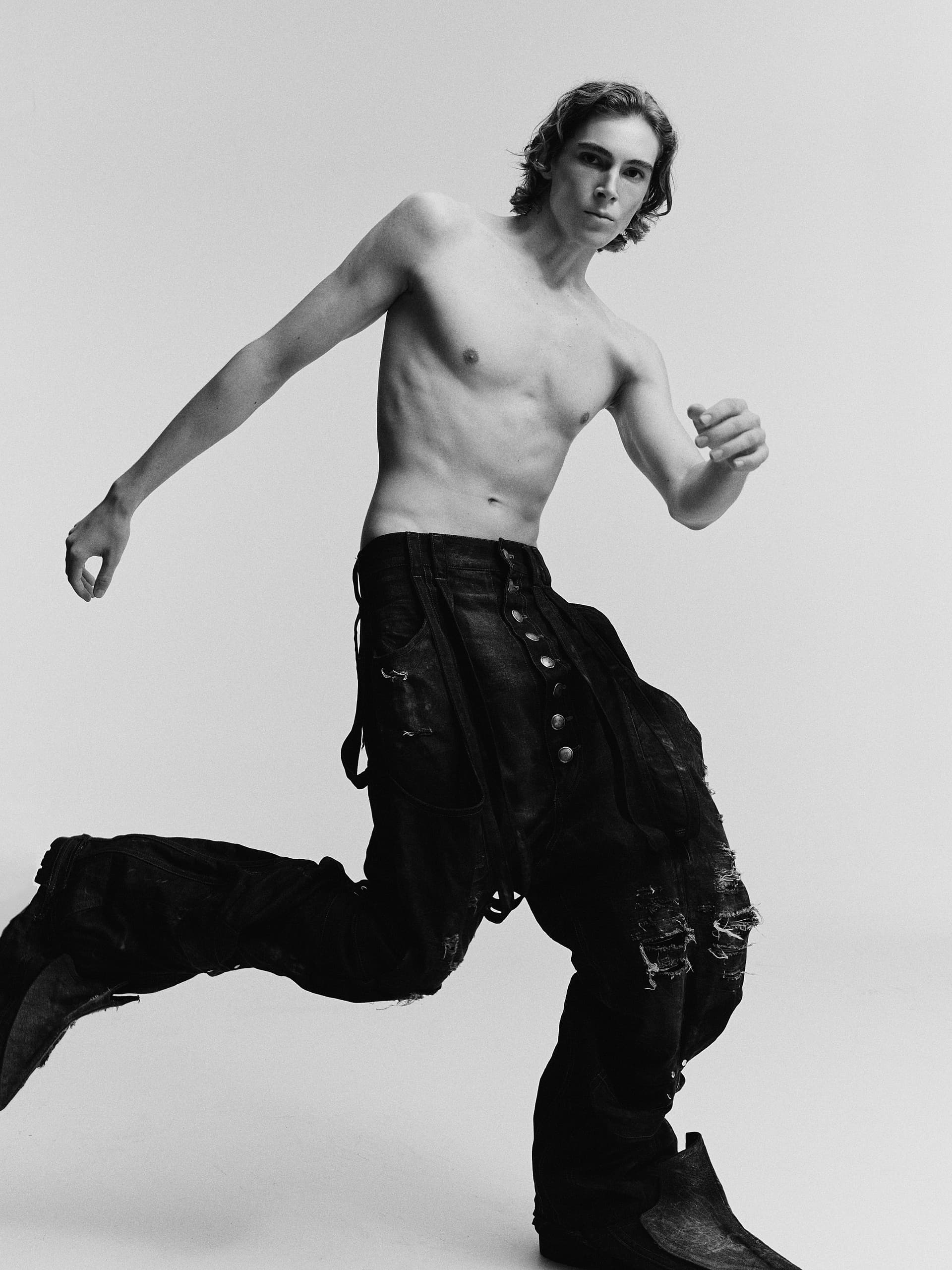 Black and white photo of a stylish, shirtless man in oversized pants.