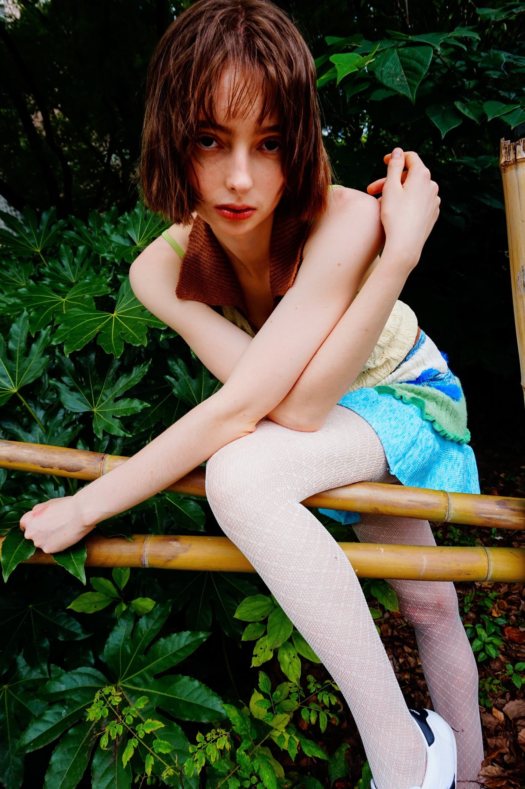 Person in colorful outfit sitting on bamboo amidst lush green foliage.