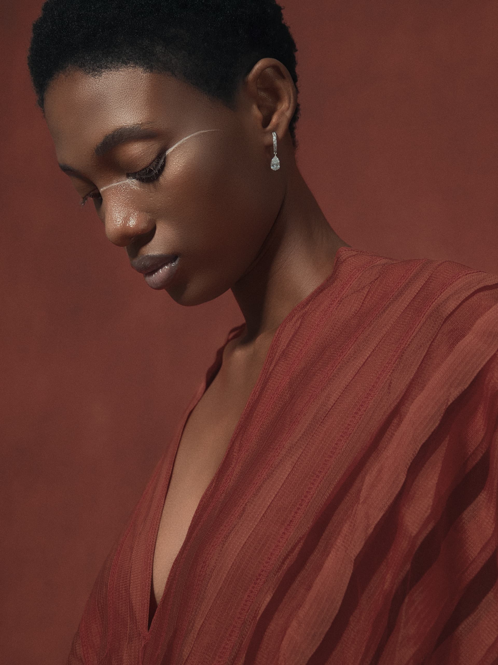 Elegant woman in red dress with earring against a textured background.