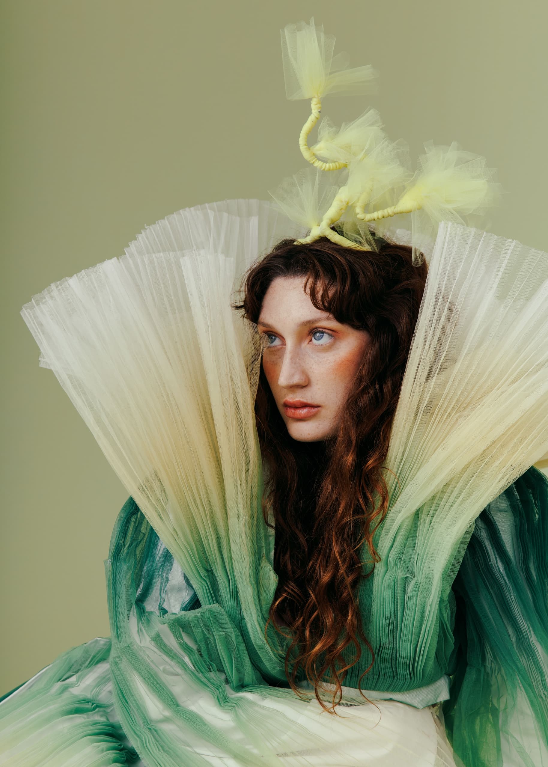 Fashion model in green and yellow avant-garde outfit with dramatic pleated design.