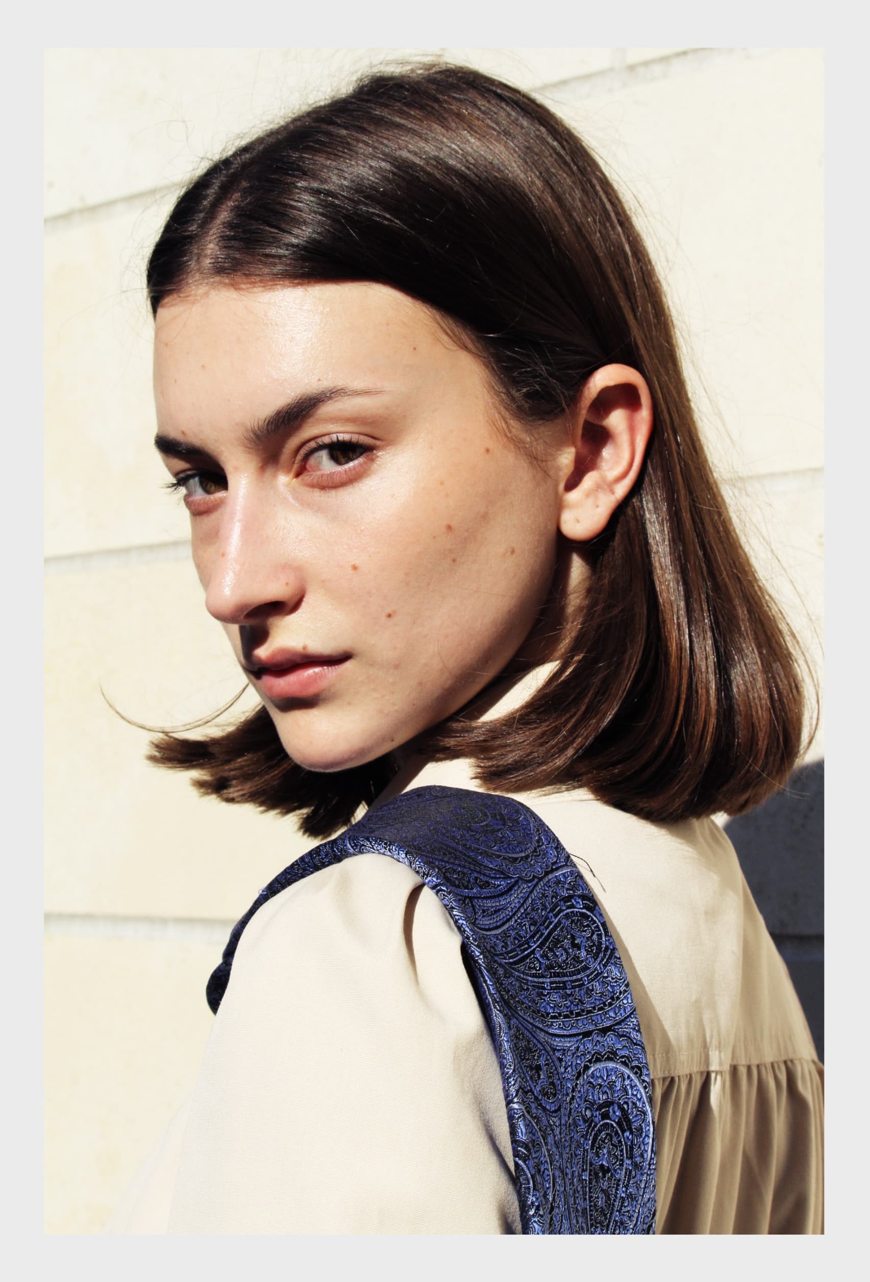 Side profile of a woman in sunlight, wearing a beige shirt with blue patterned fabric.