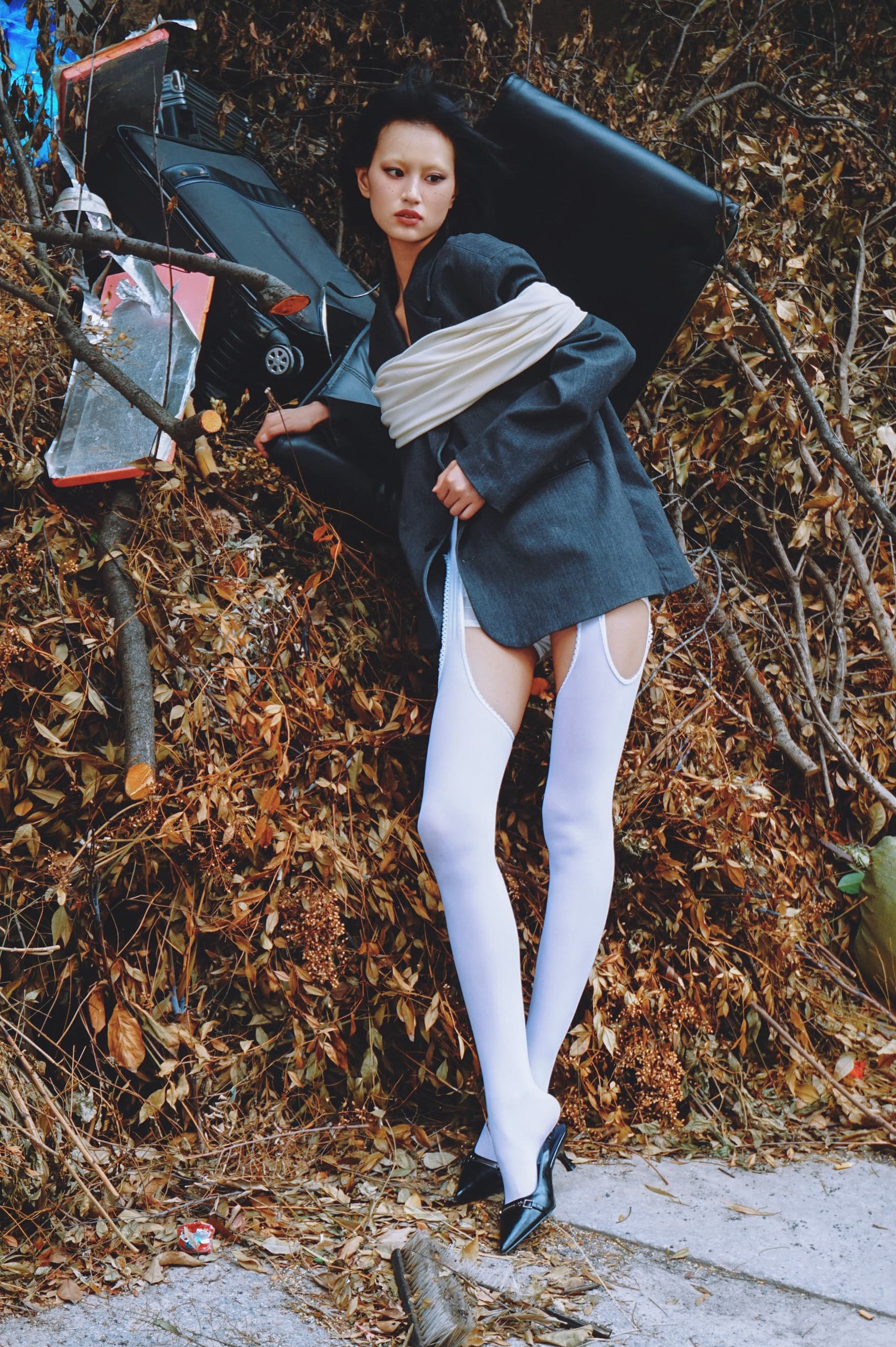 Fashion model in edgy attire poses against autumn foliage and debris.