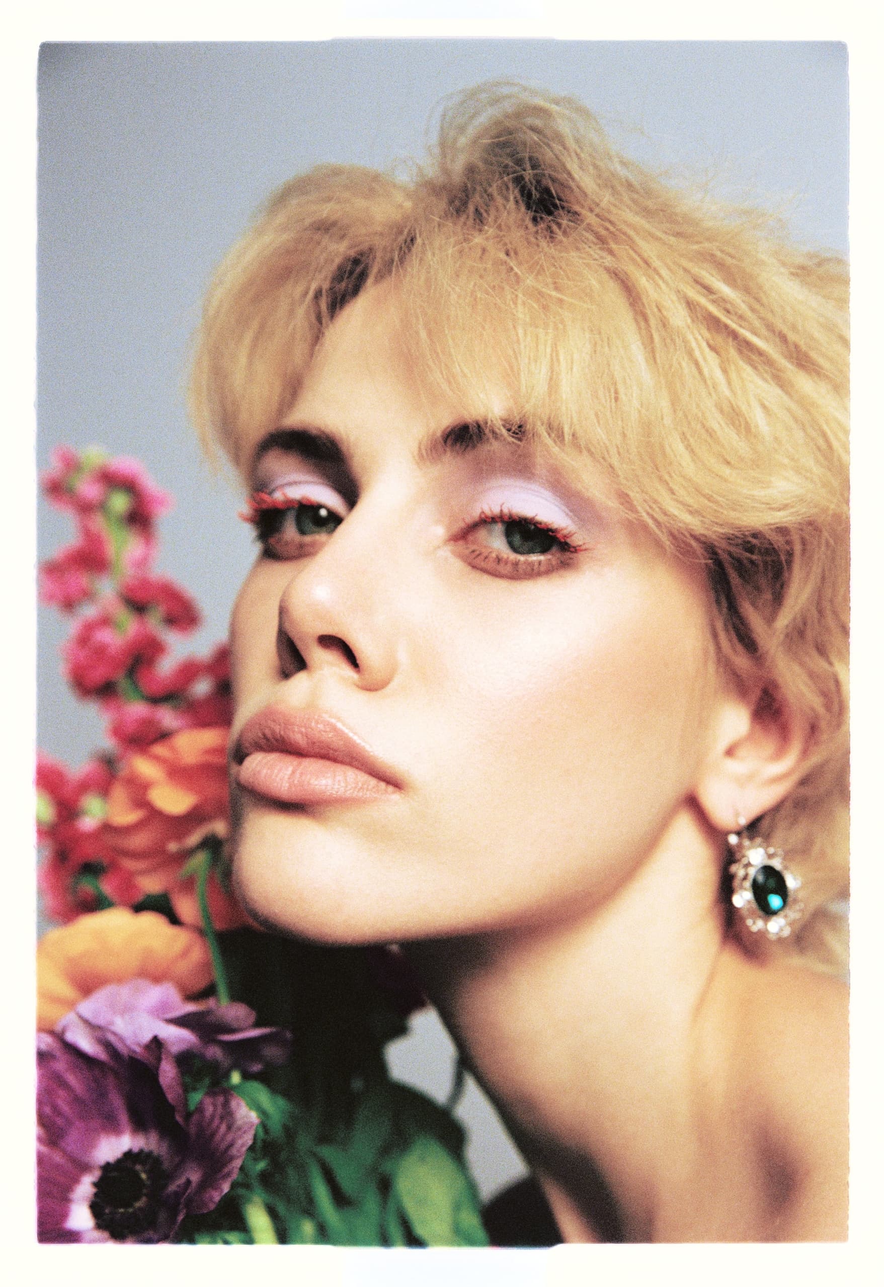 Woman with flowers and bold eye makeup gazes intensely.