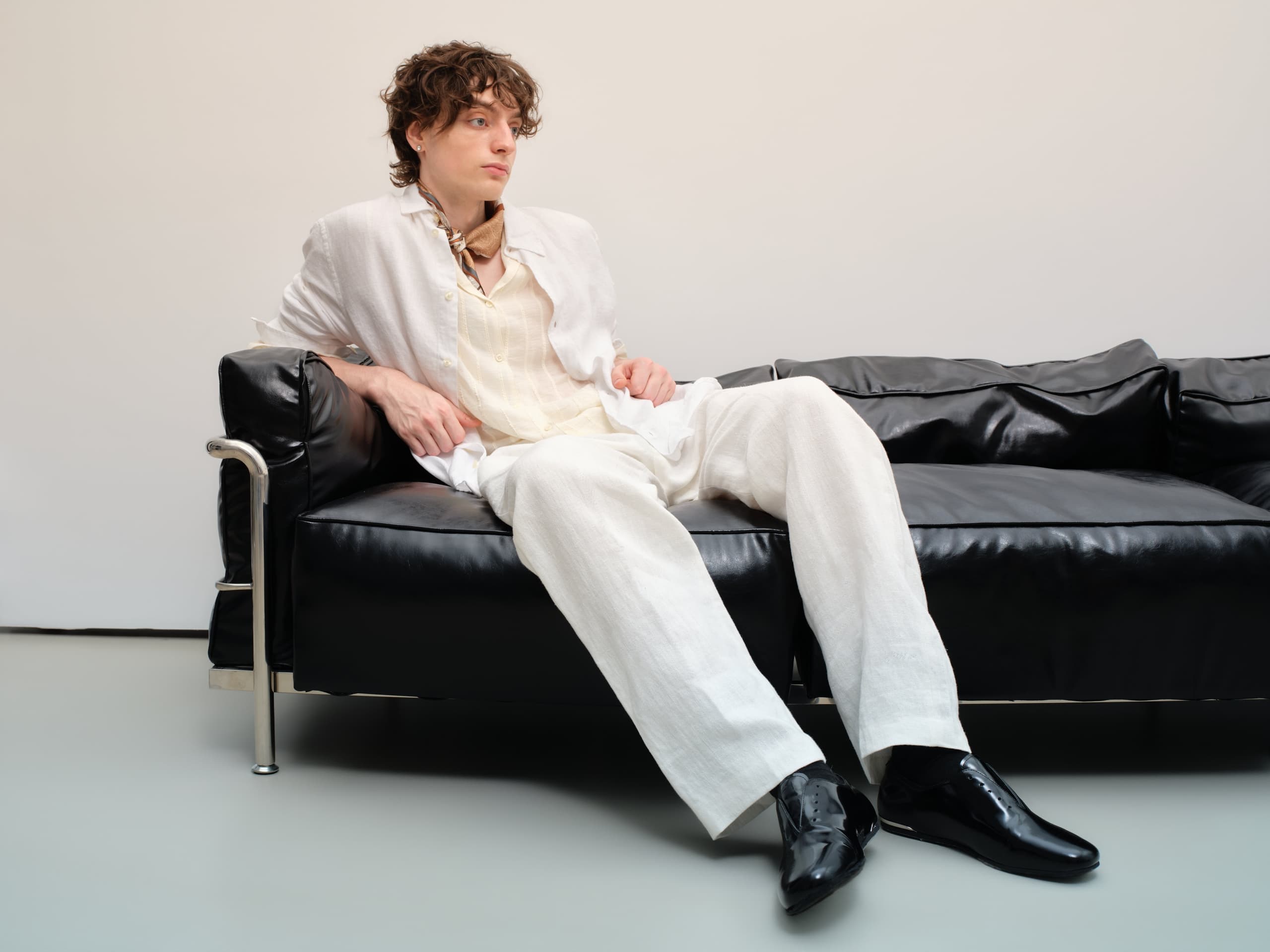 Man in stylish white outfit sitting on a black leather sofa.