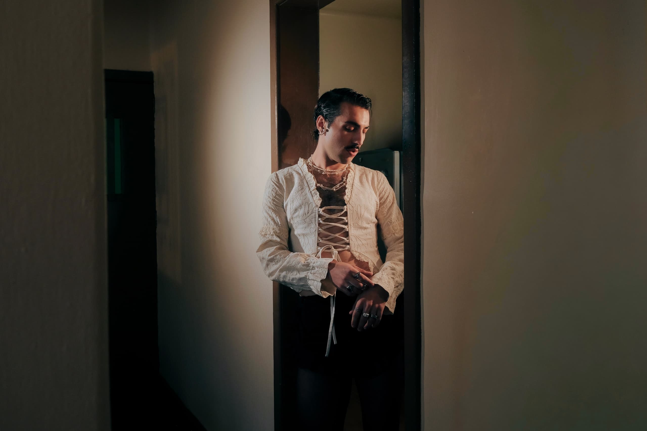 Person in lace-up top leans against a dimly lit doorframe.
