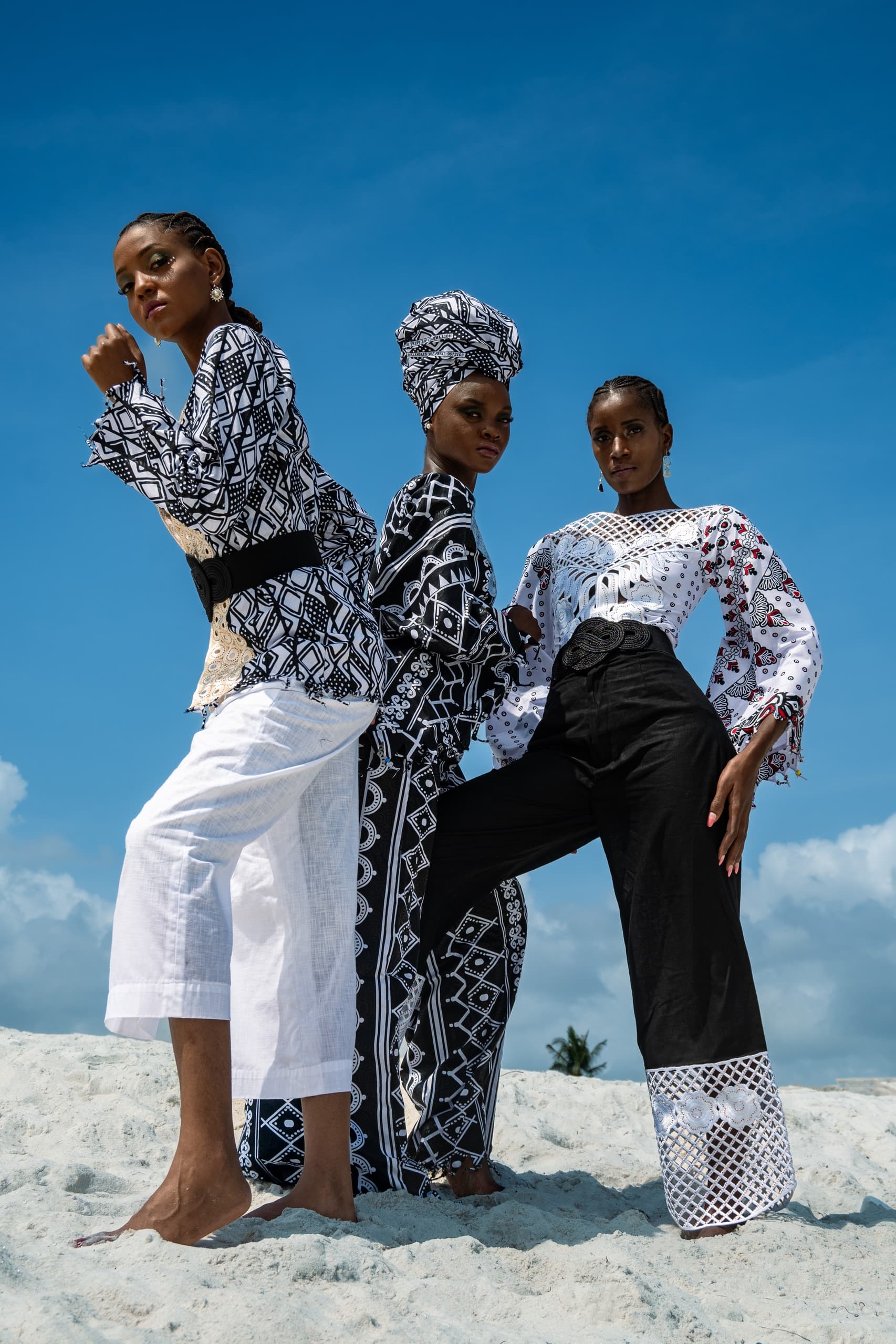 Three models in vibrant patterned outfits on a beach under a clear blue sky.