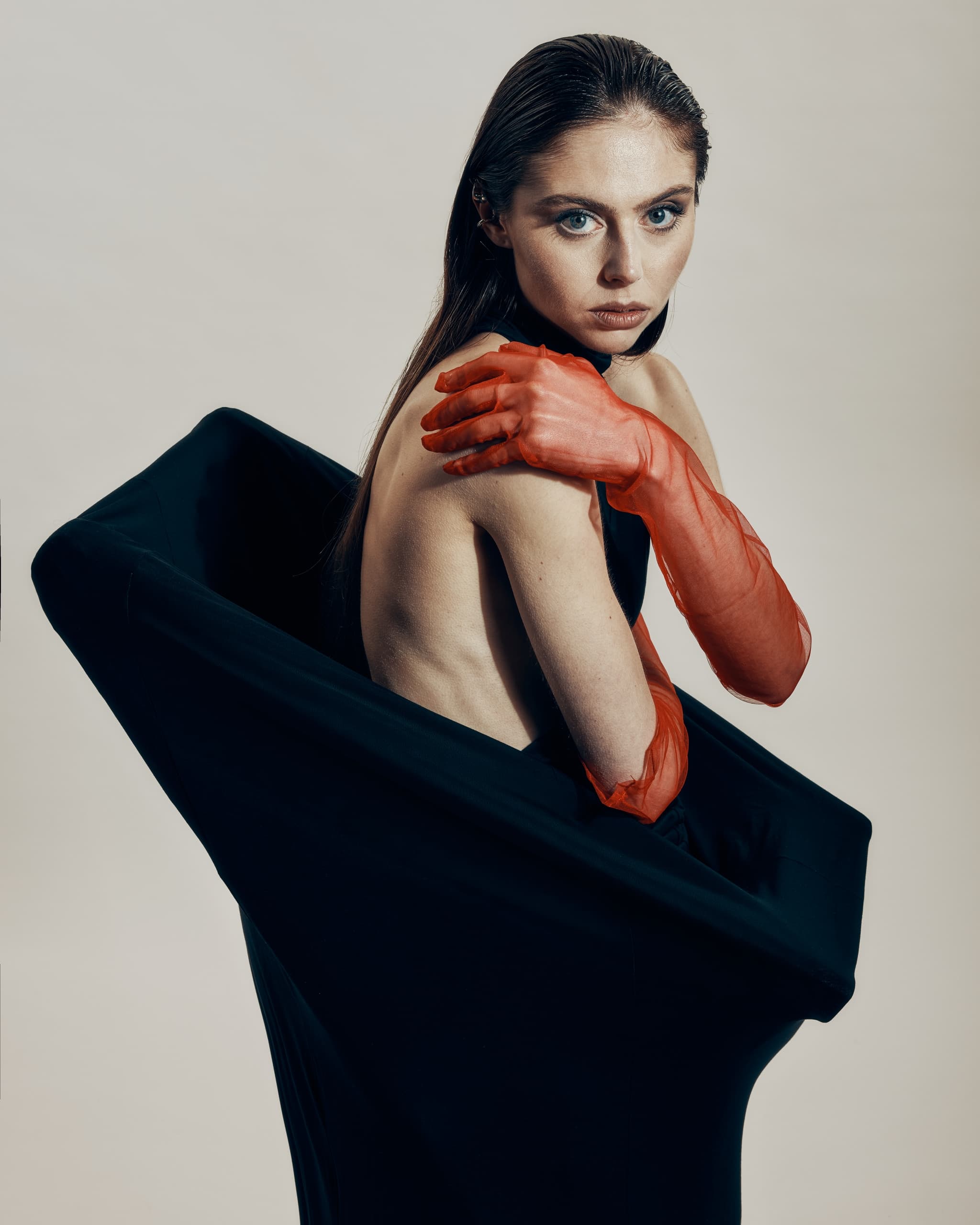 Woman in stylish outfit and red gloves posing artistically on neutral background.