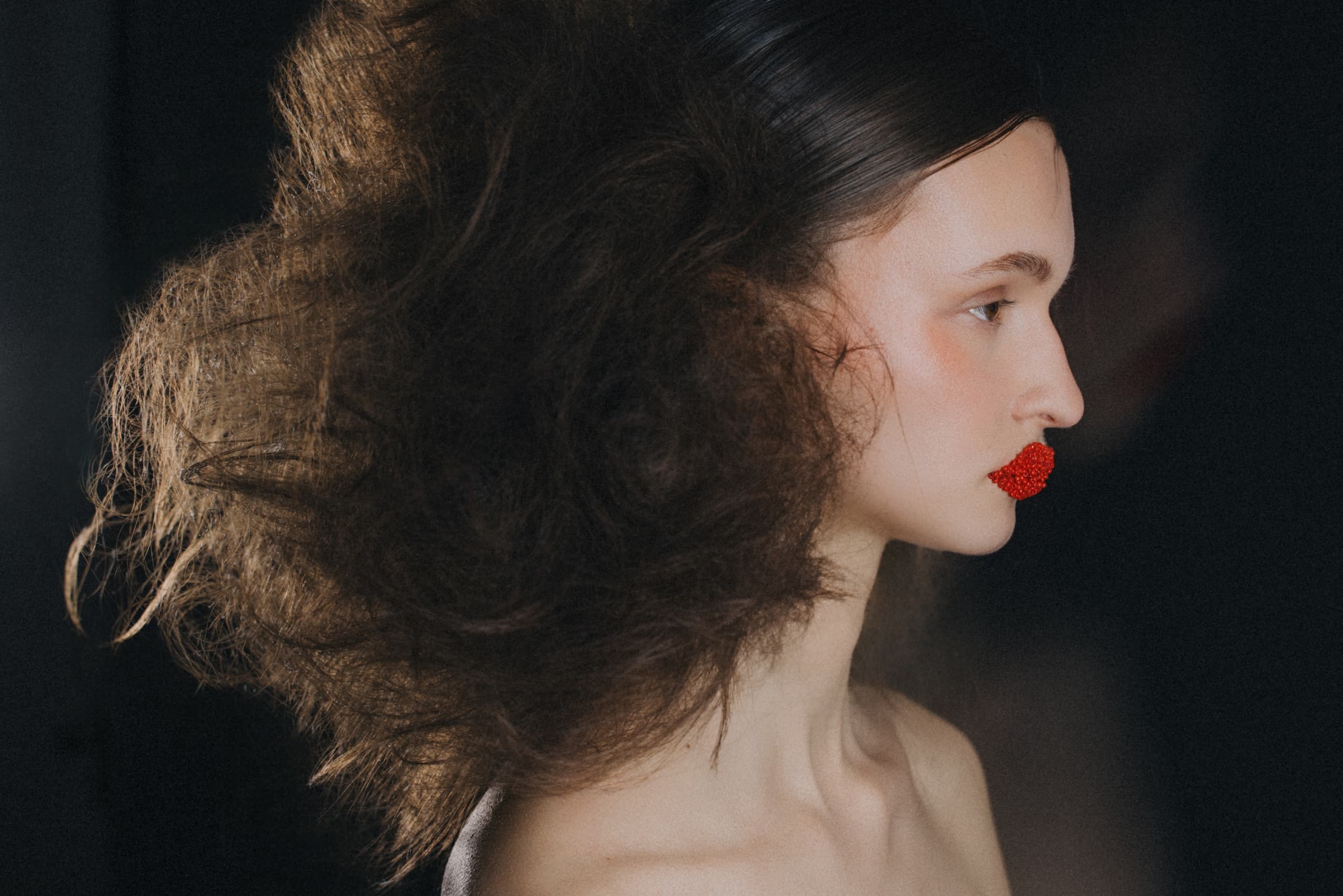 Fashion model with voluminous hair and bold red textured lip artistry.