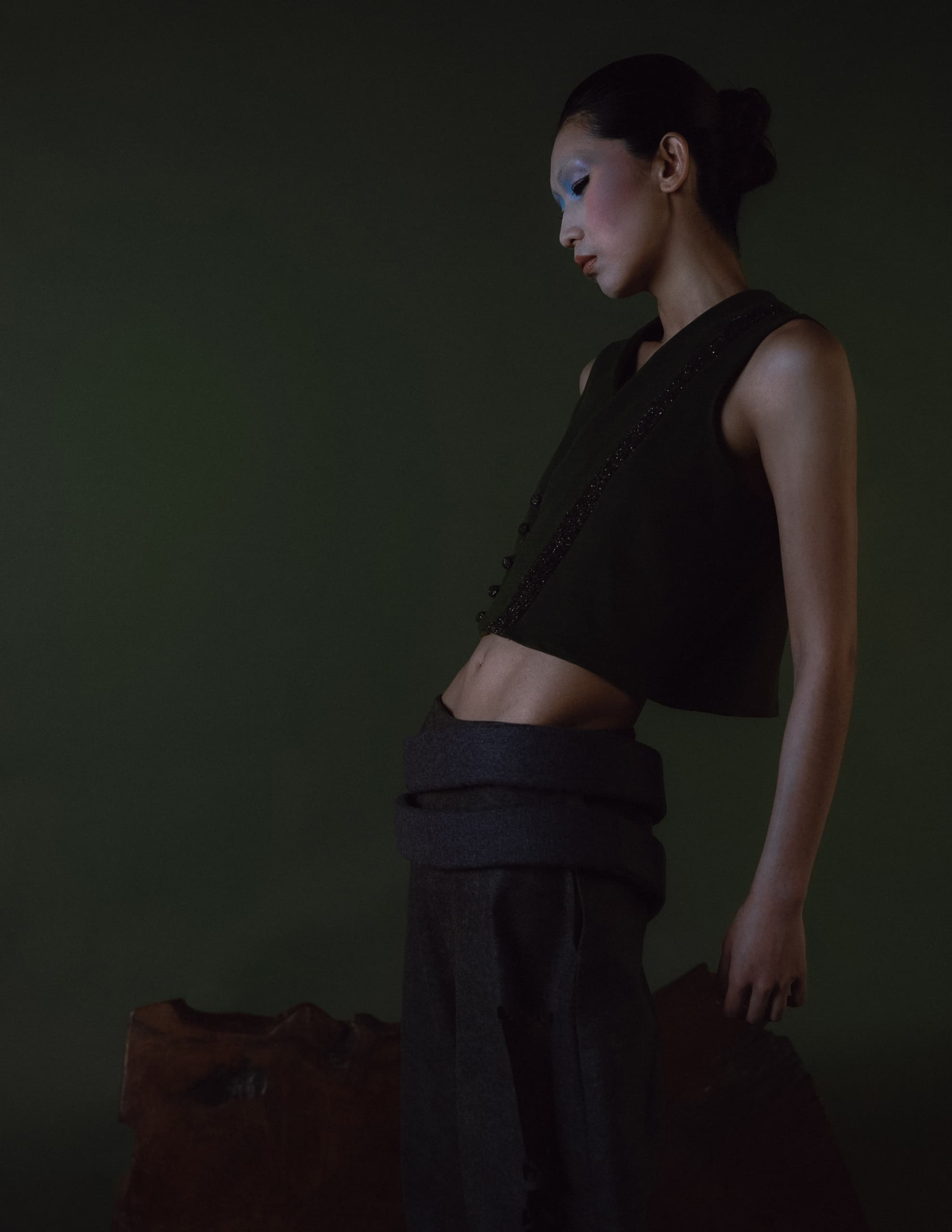 Fashion model in dark attire poses against green backdrop.