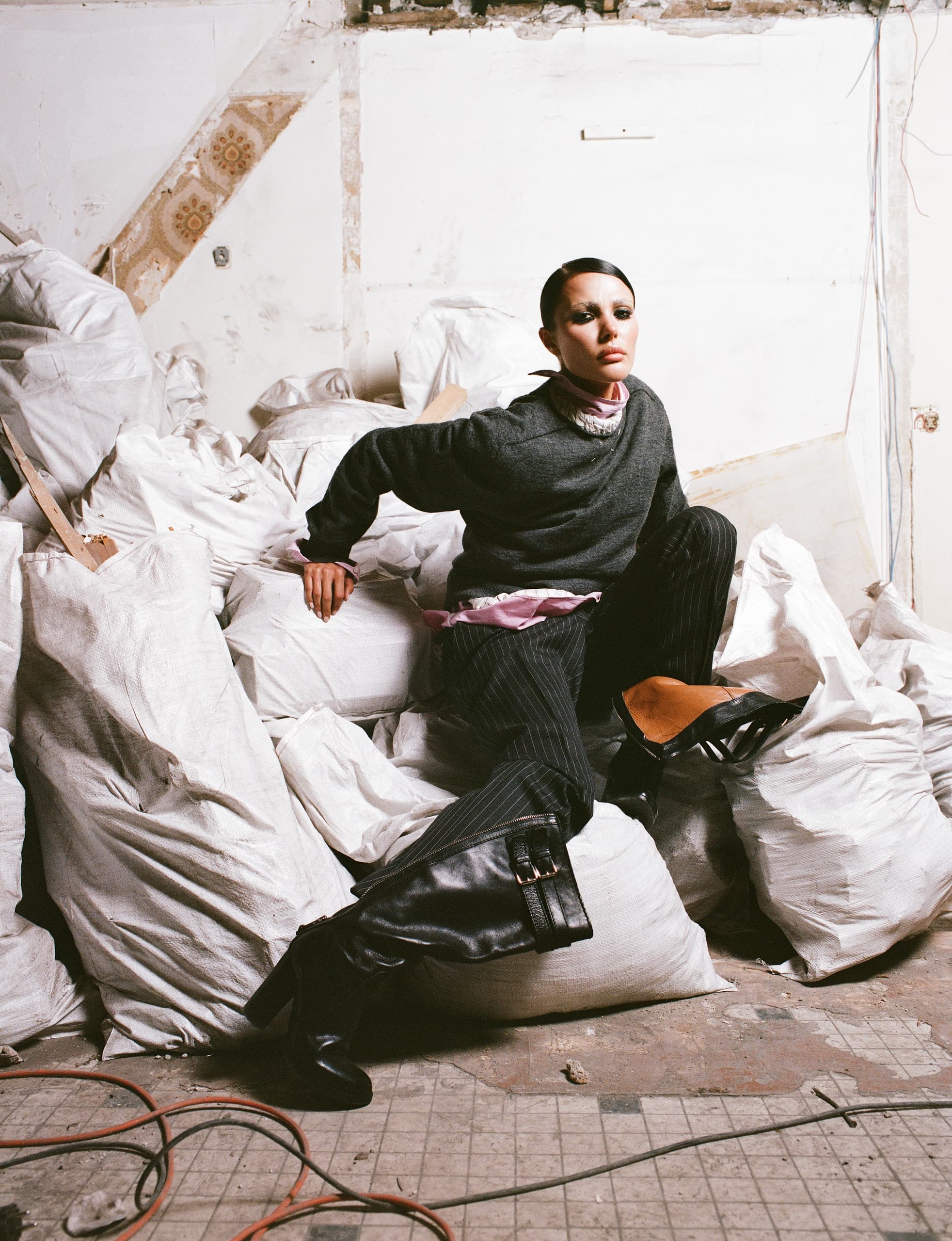 Fashion model in edgy attire posing on construction site with rubble bags.