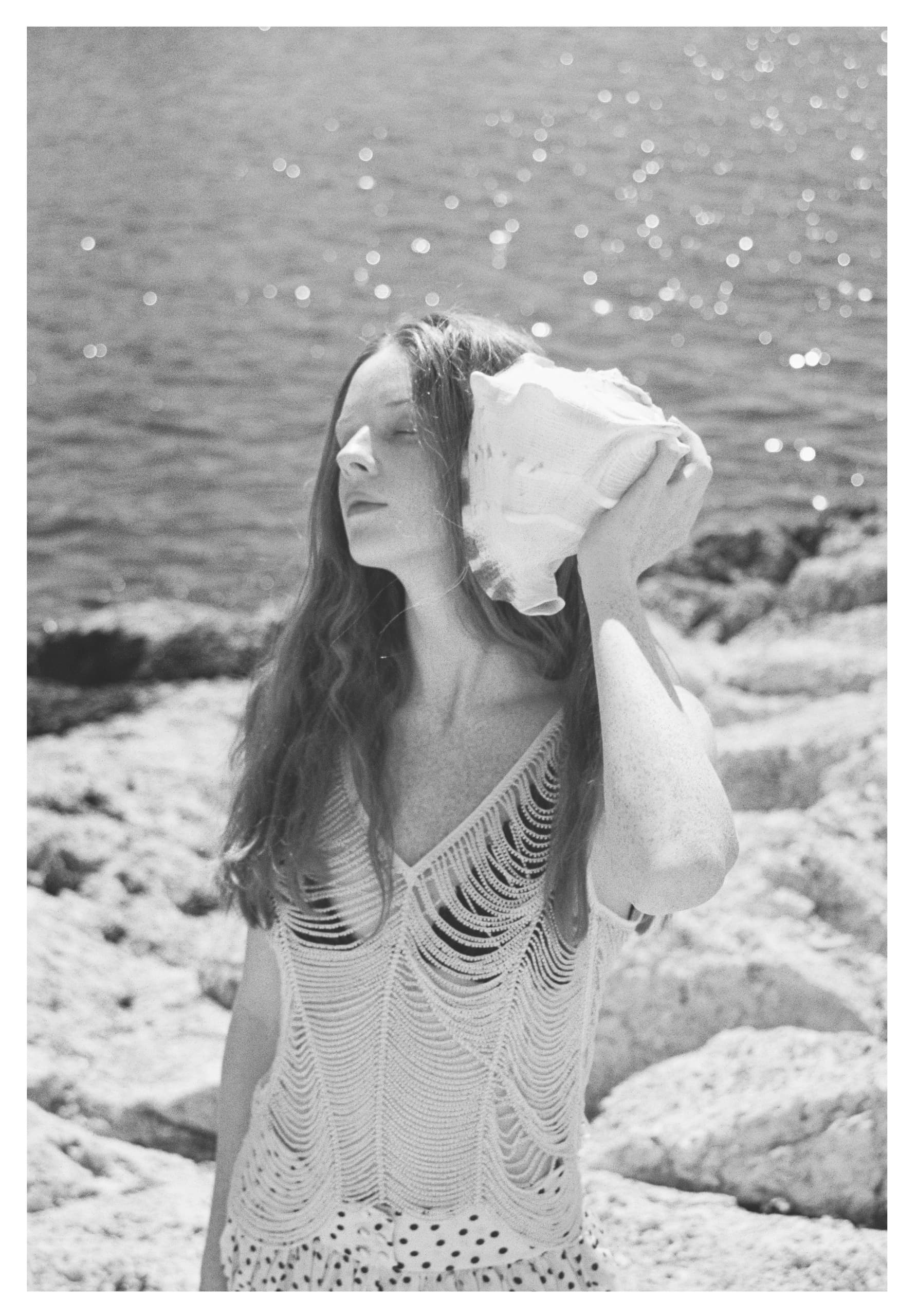 Woman with long hair holding a seashell at the rocky seaside.