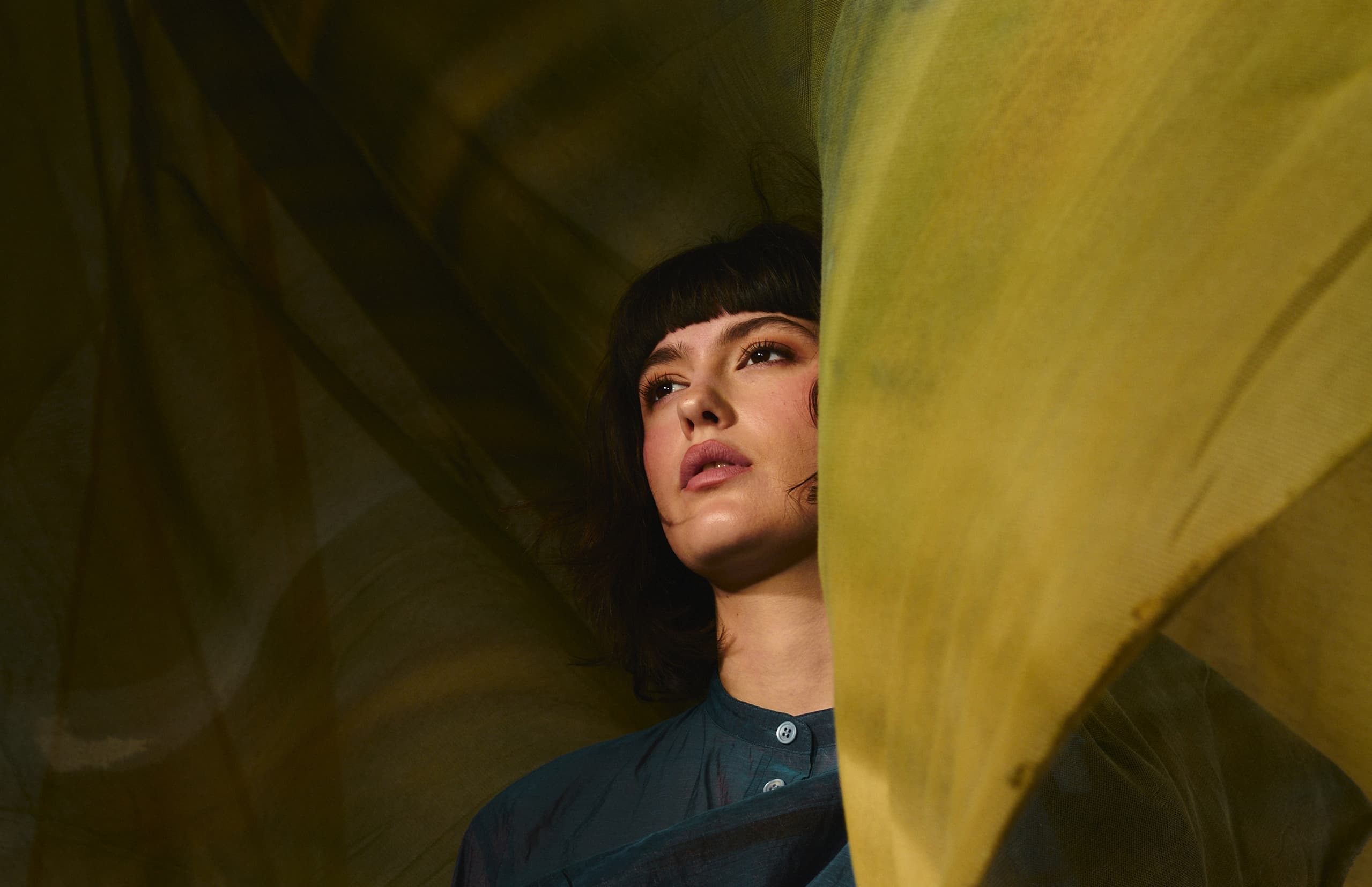 Woman gazing through translucent fabric with focused expression.