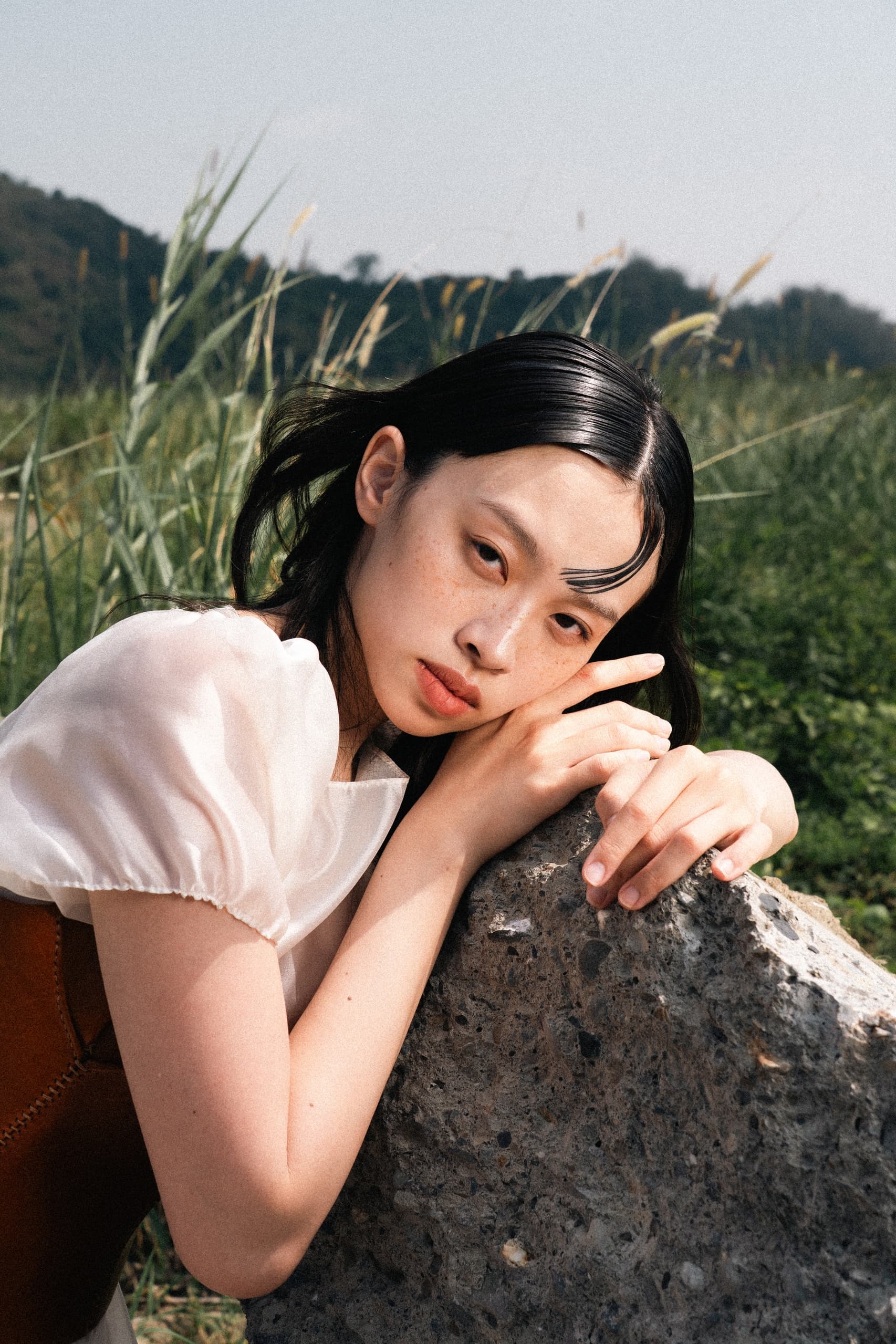 Woman with long hair posing thoughtfully by rock in natural setting.
