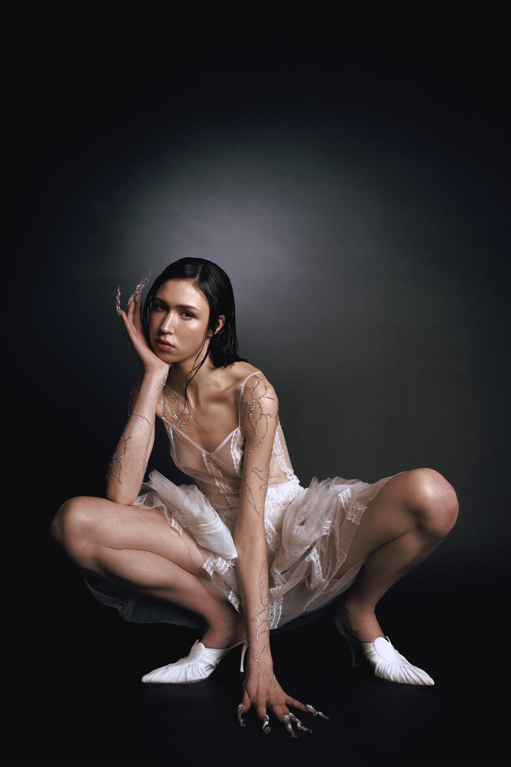 Model in delicate dress with artistic nails and crystal body art, striking a pose.