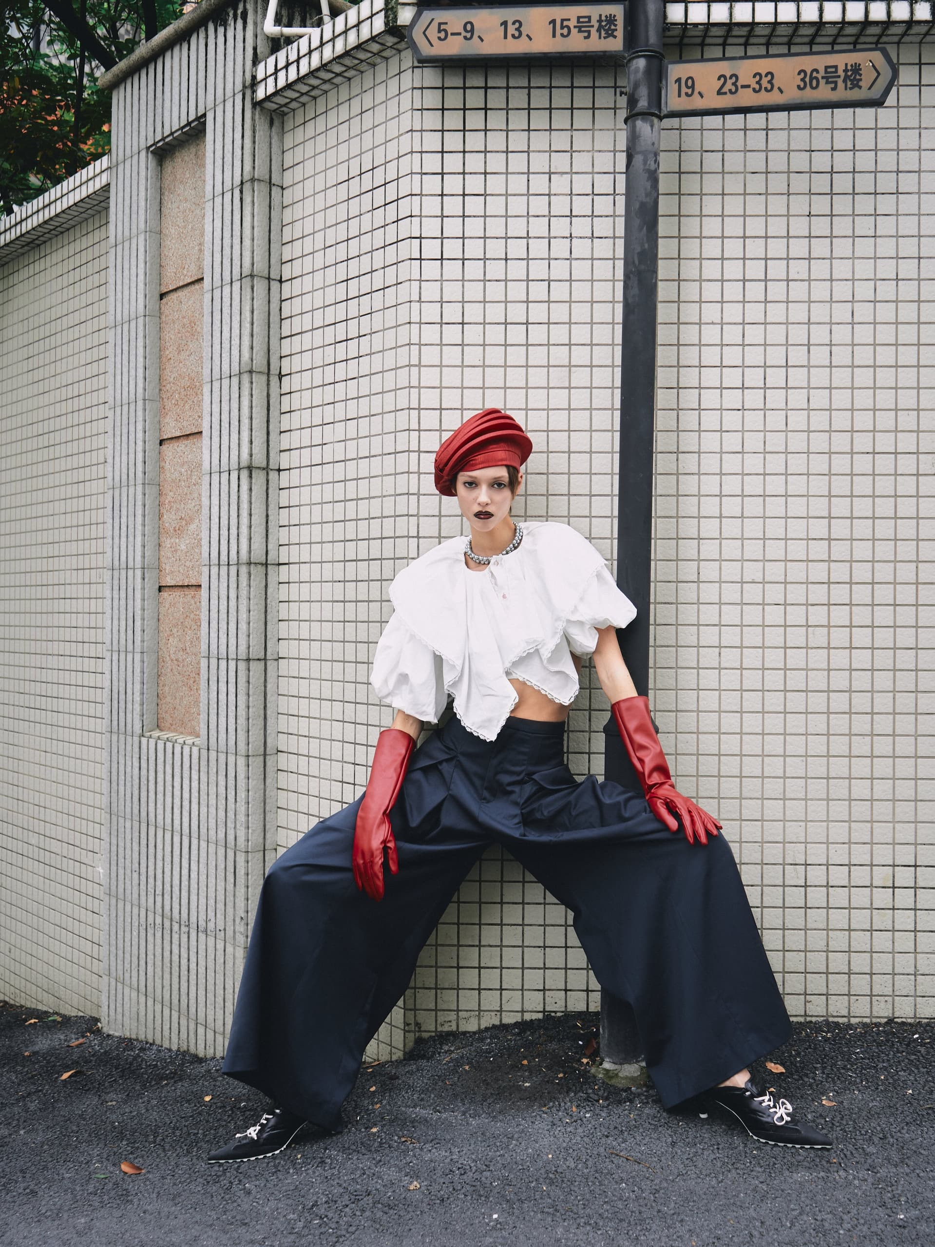 Fashionable person in bold outfit poses in urban setting, styled with red gloves and hat.
