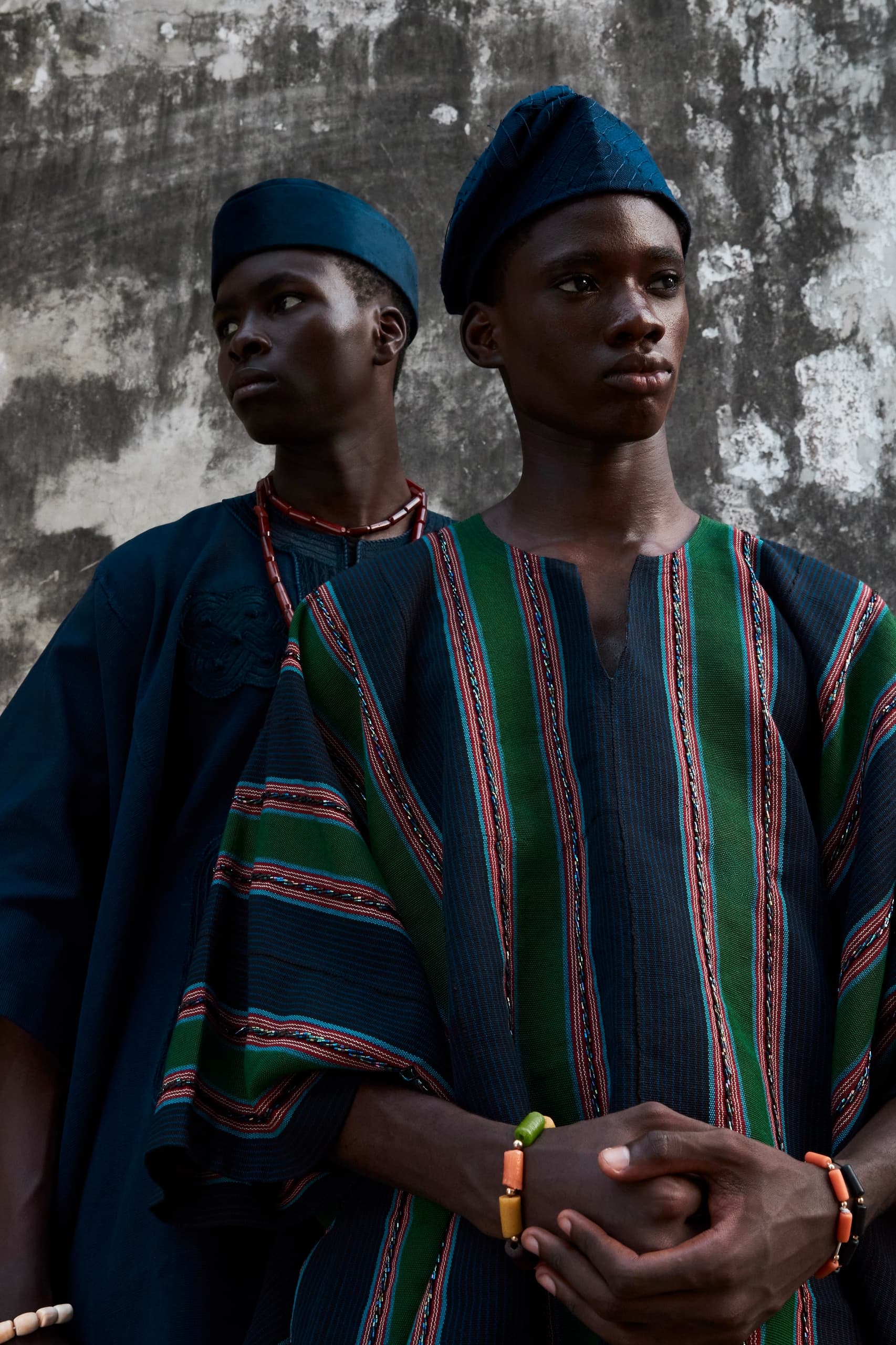 Two men in traditional colorful clothing against a textured wall.