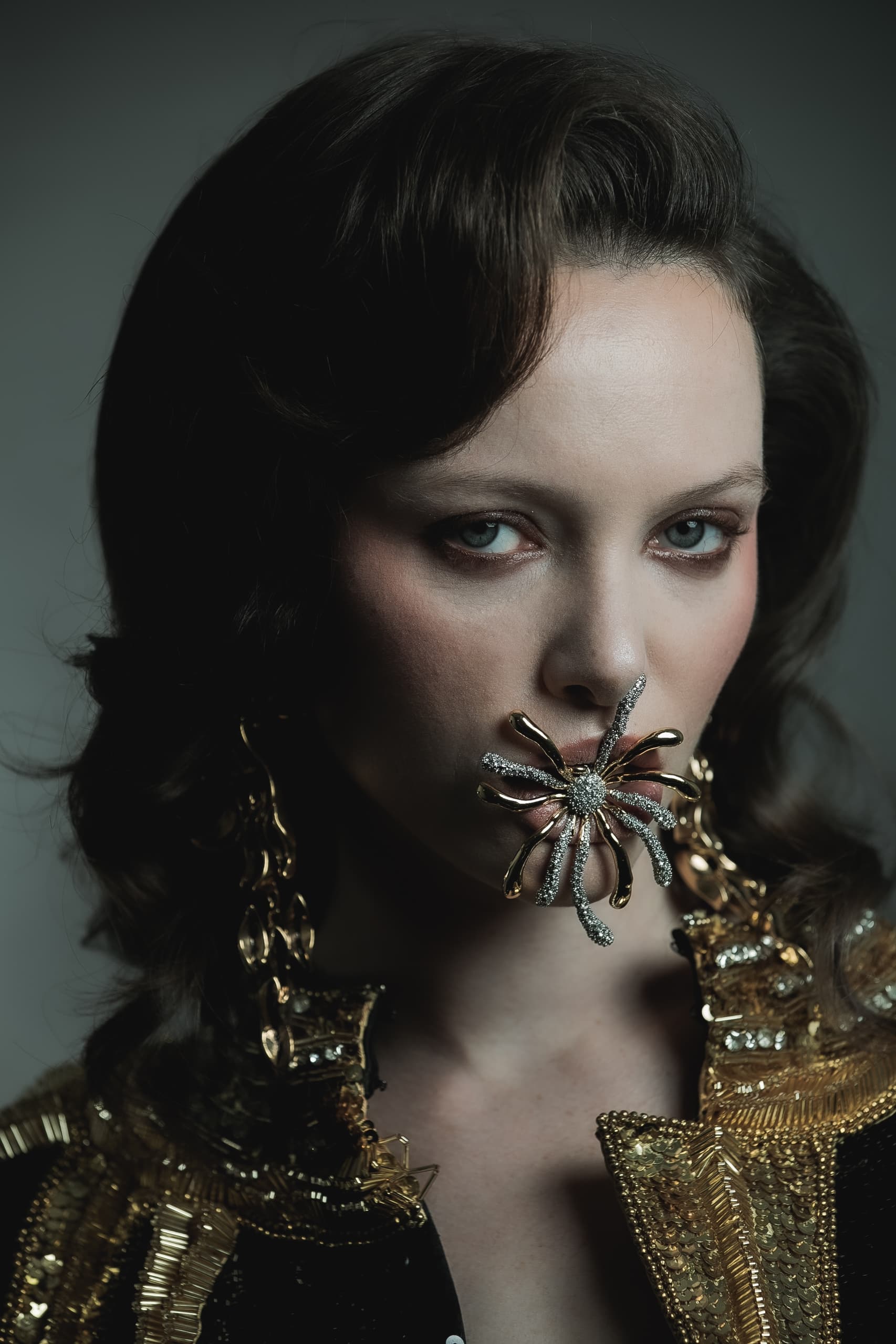 Woman with bold spider jewelry on face, wearing ornate gold and black attire.