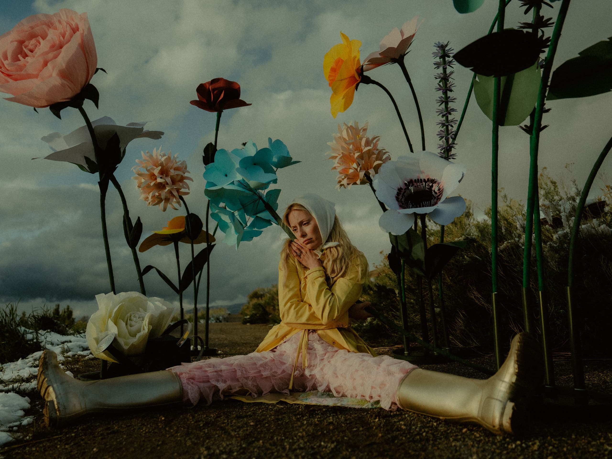 Person sitting among oversized colorful flowers in a whimsical outdoor setting.