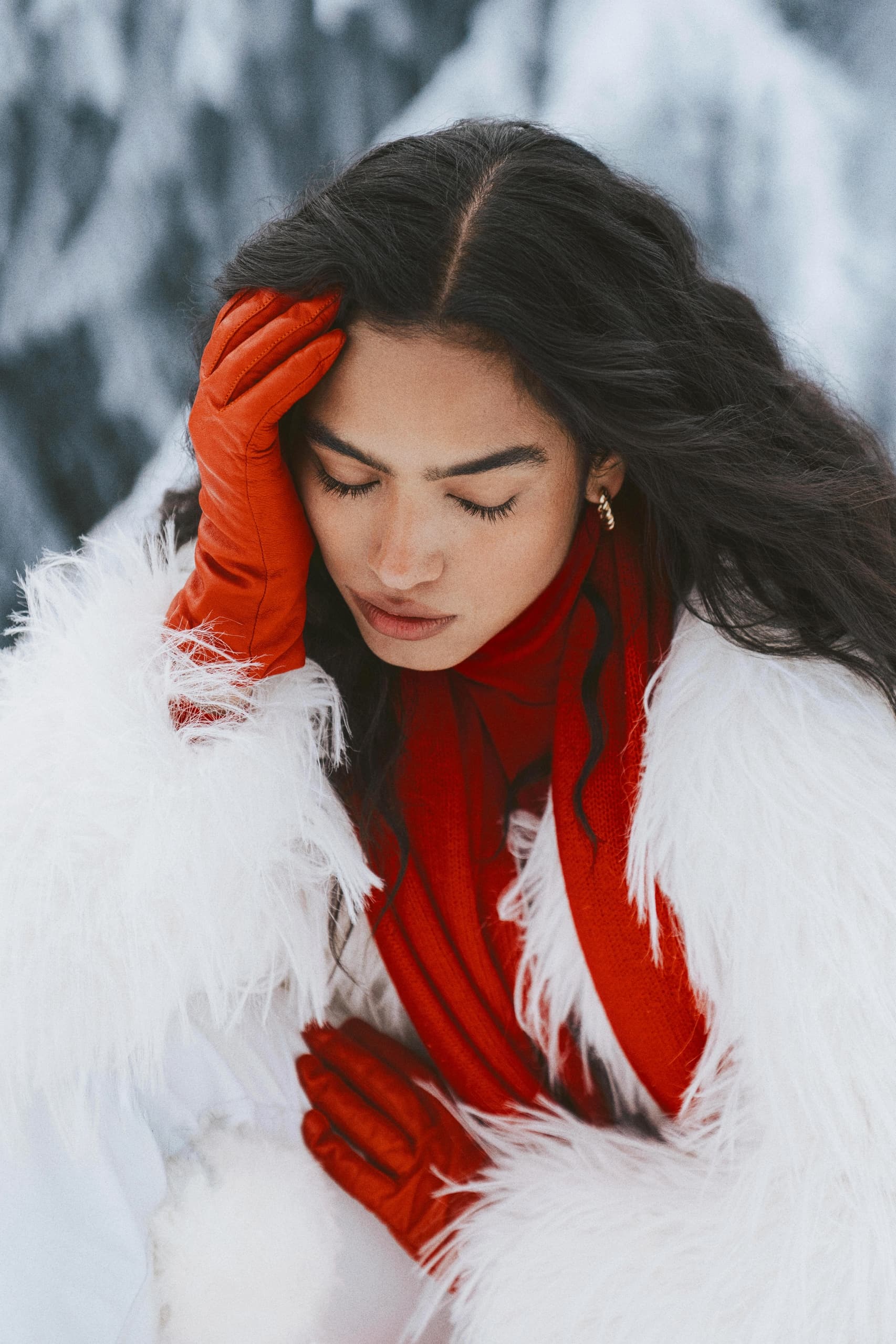 Woman in red gloves and white fur coat in snowy setting, eyes closed.