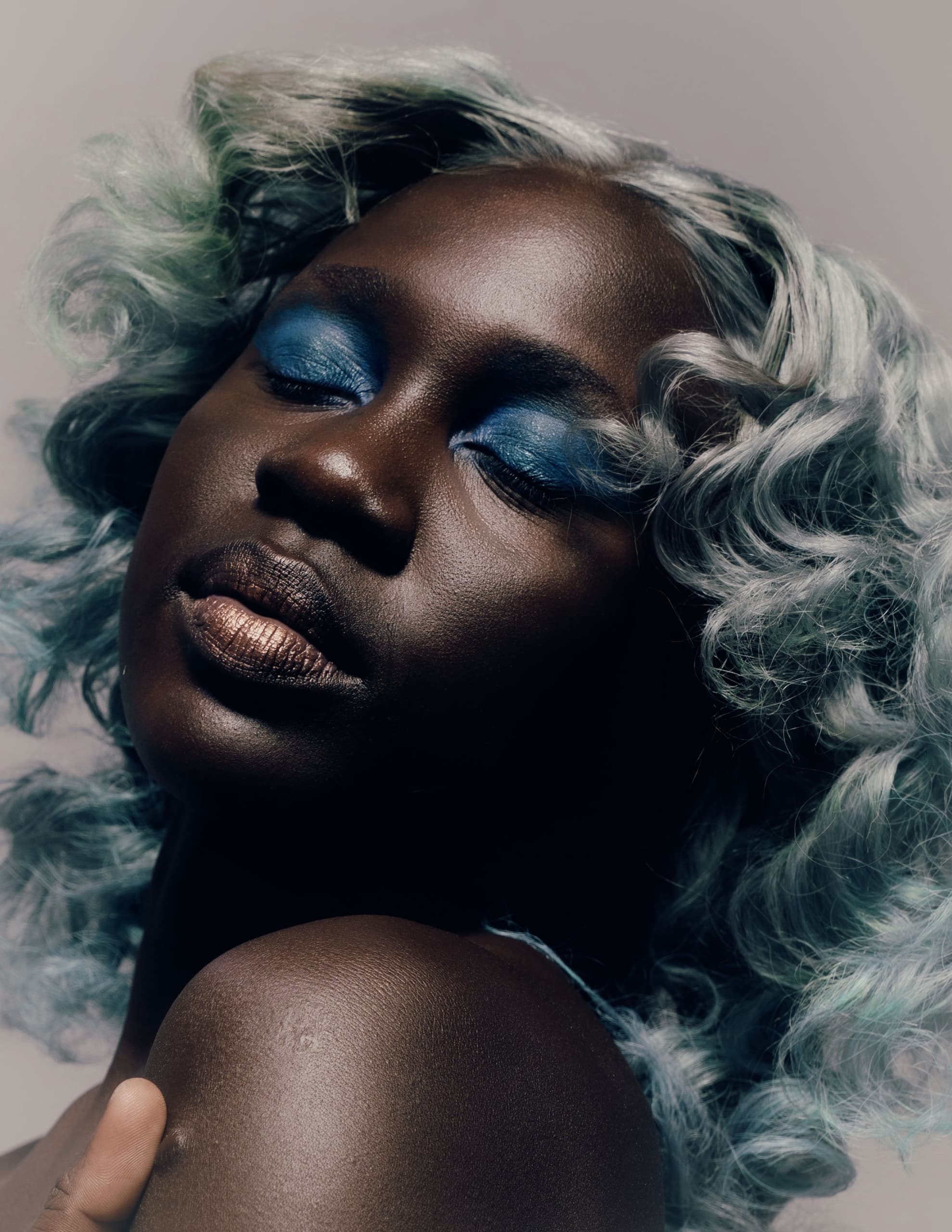 Model with blue eye makeup and silver curly hair in a dramatic pose.