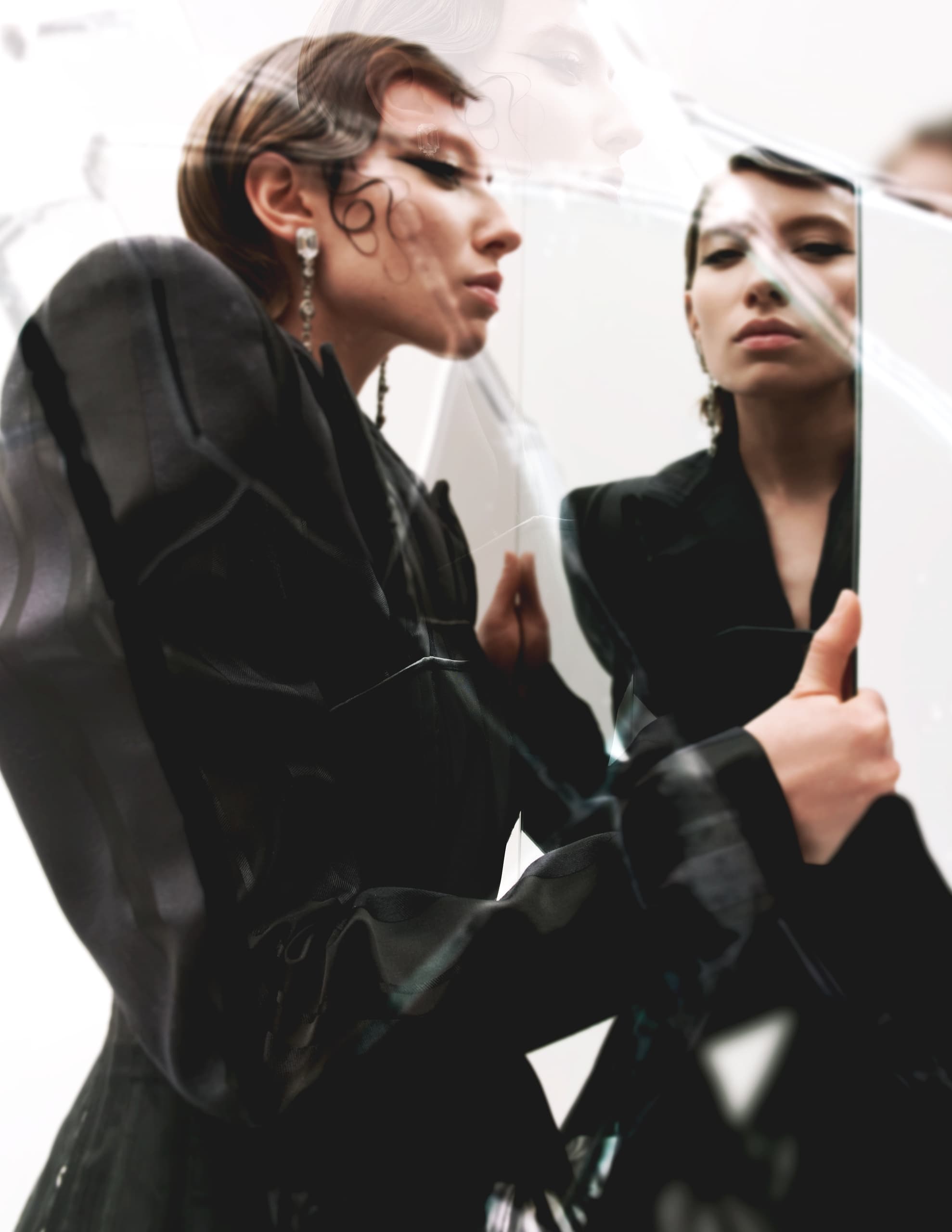 Fashionable woman gazing at reflection in mirror, wearing stylish black attire.