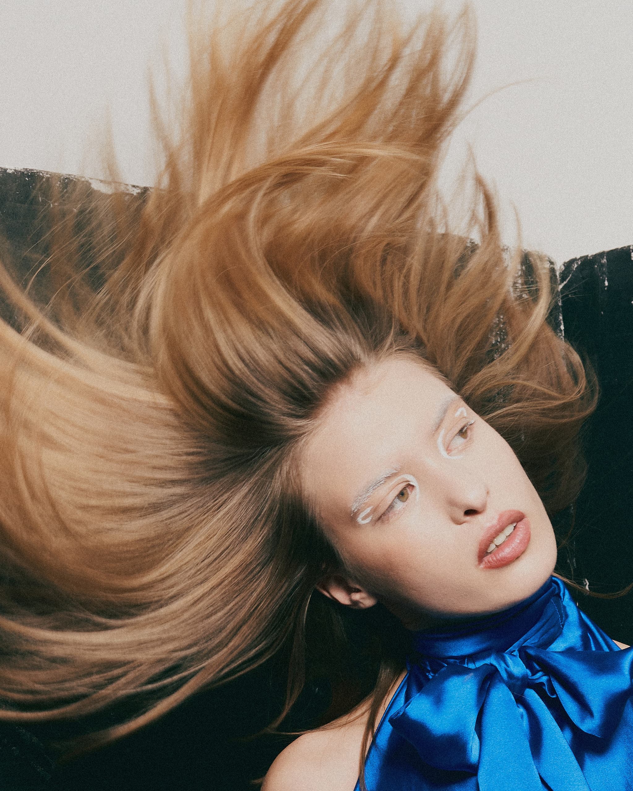 Woman with flowing hair, vibrant blue scarf, and unique makeup in dynamic pose.