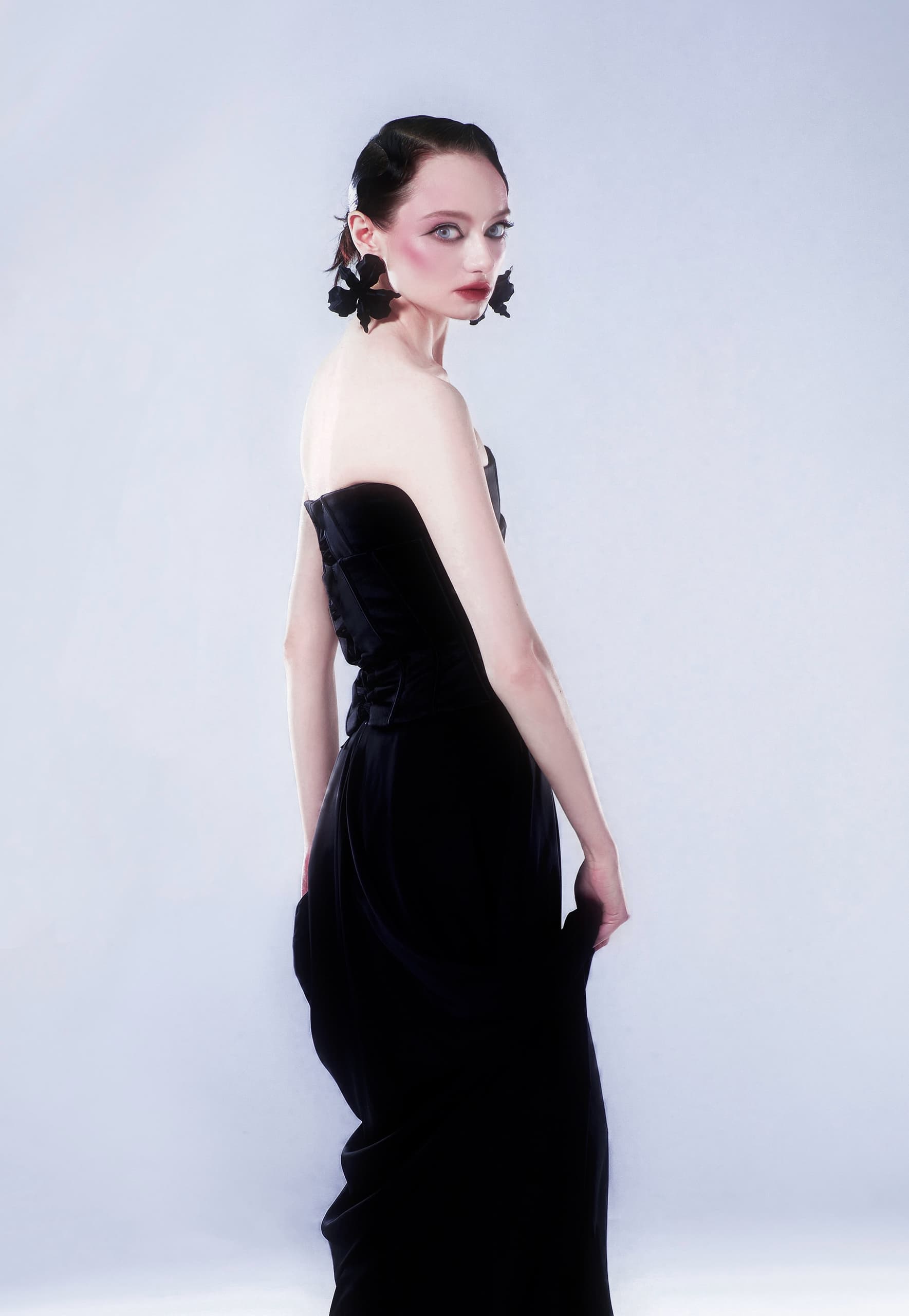 Elegant model in a black strapless gown, showcasing chic fashion style.