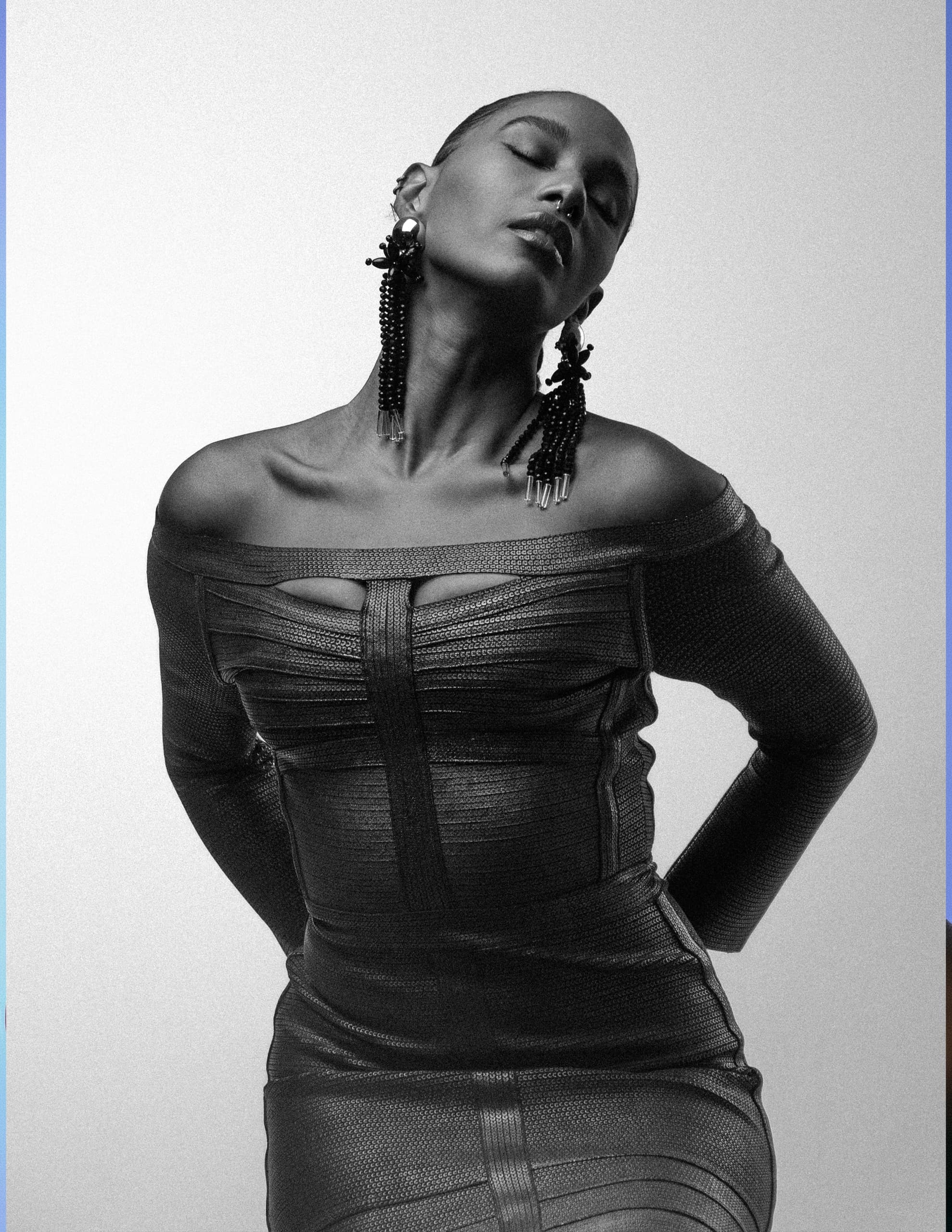 Monochrome portrait of a woman in a stylish off-shoulder dress, wearing bold earrings.