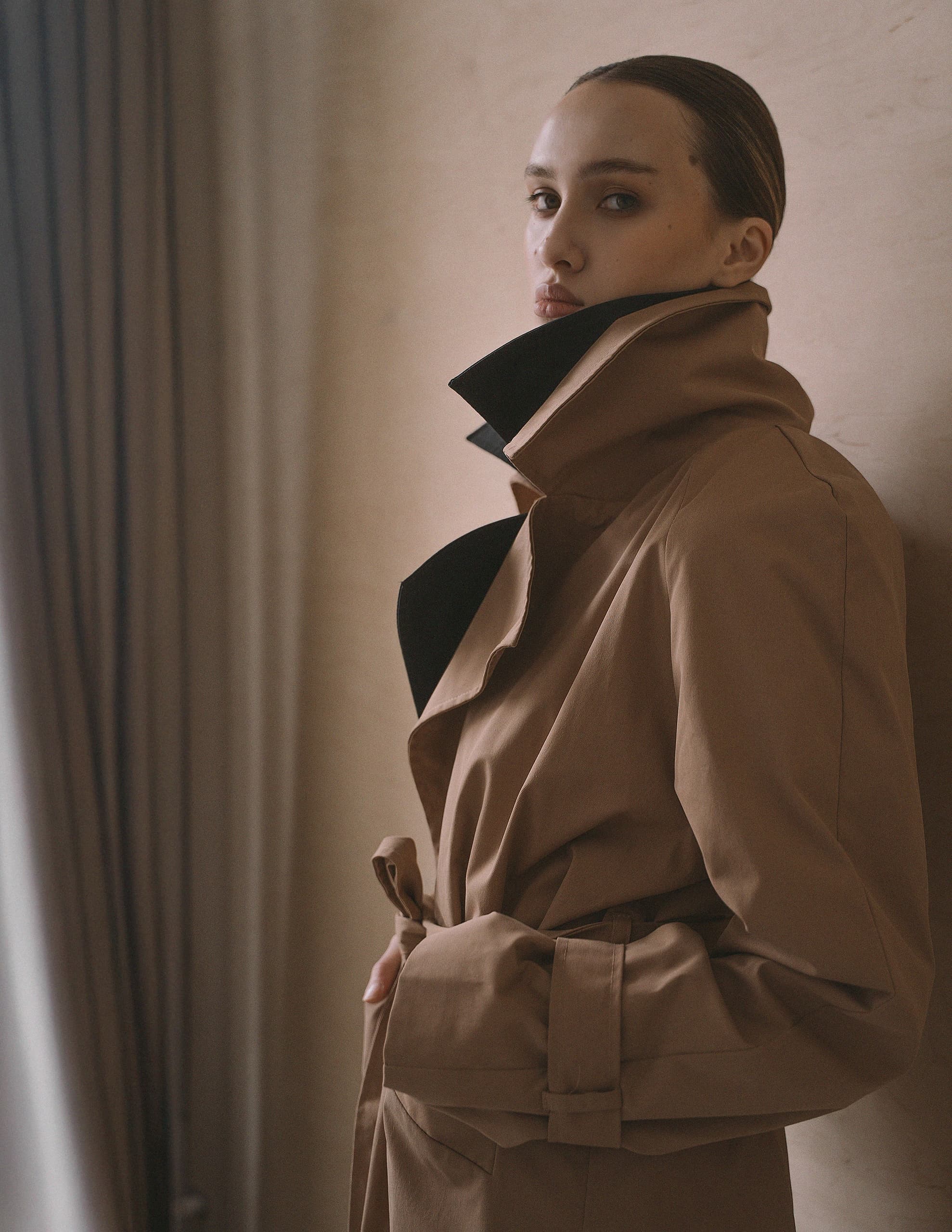 Fashion model in a stylish trench coat posing indoors with a neutral background.