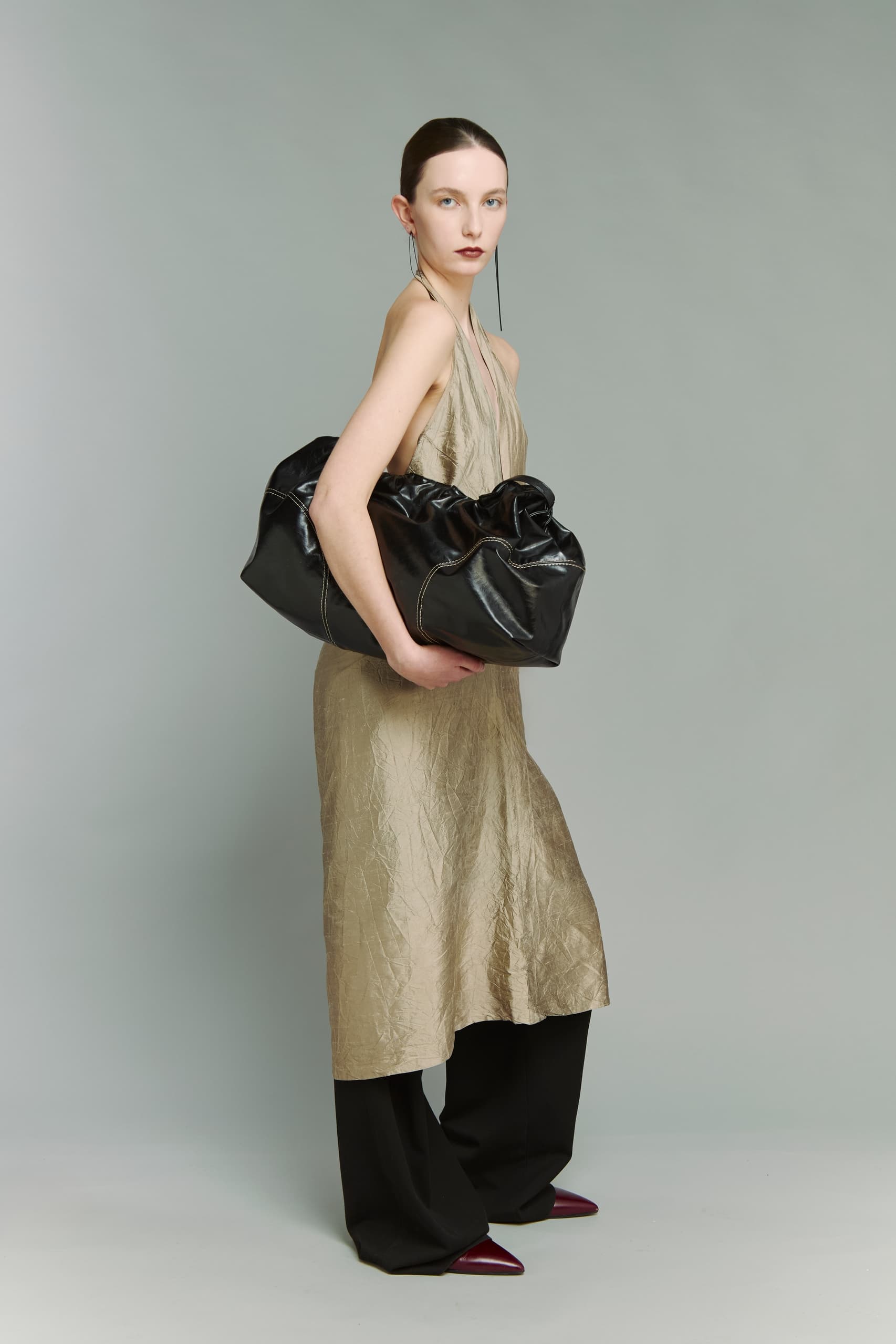 Fashionable woman modeling luxury dress and large black handbag.