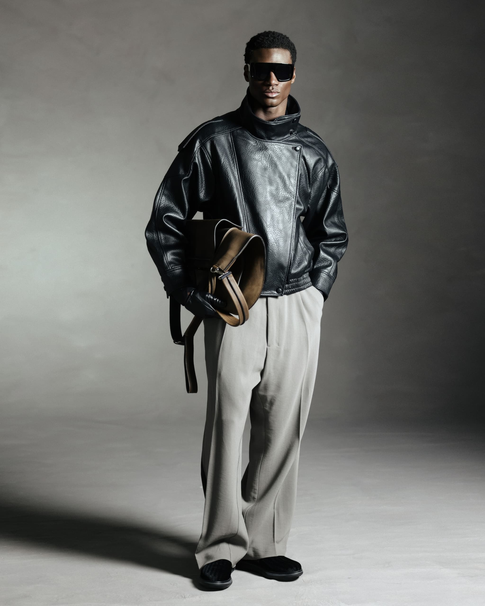 Man in leather jacket and sunglasses holding a bag, stylish fashion portrait.