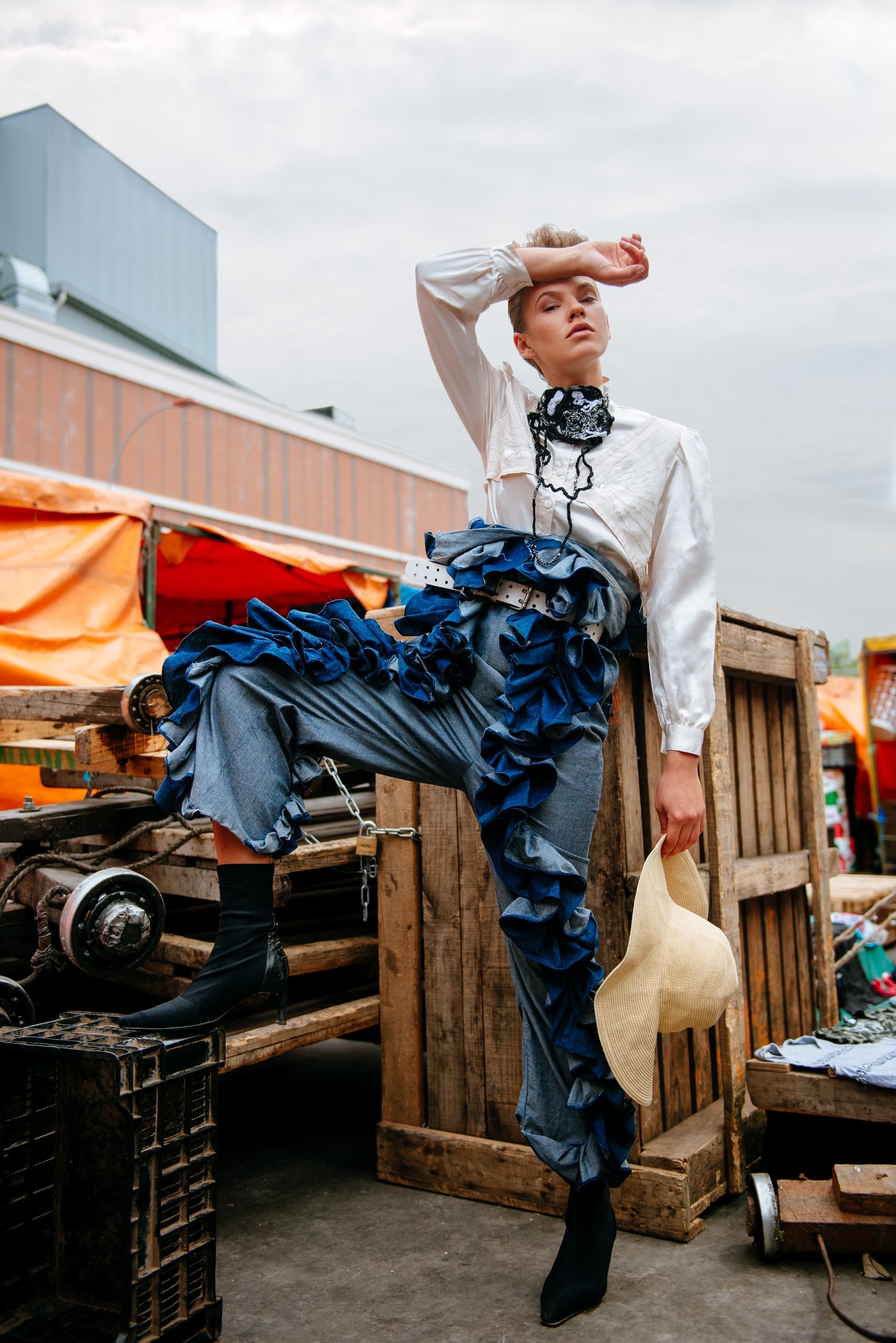 Fashionable person in ruffled outfit posing outdoors with market backdrop.