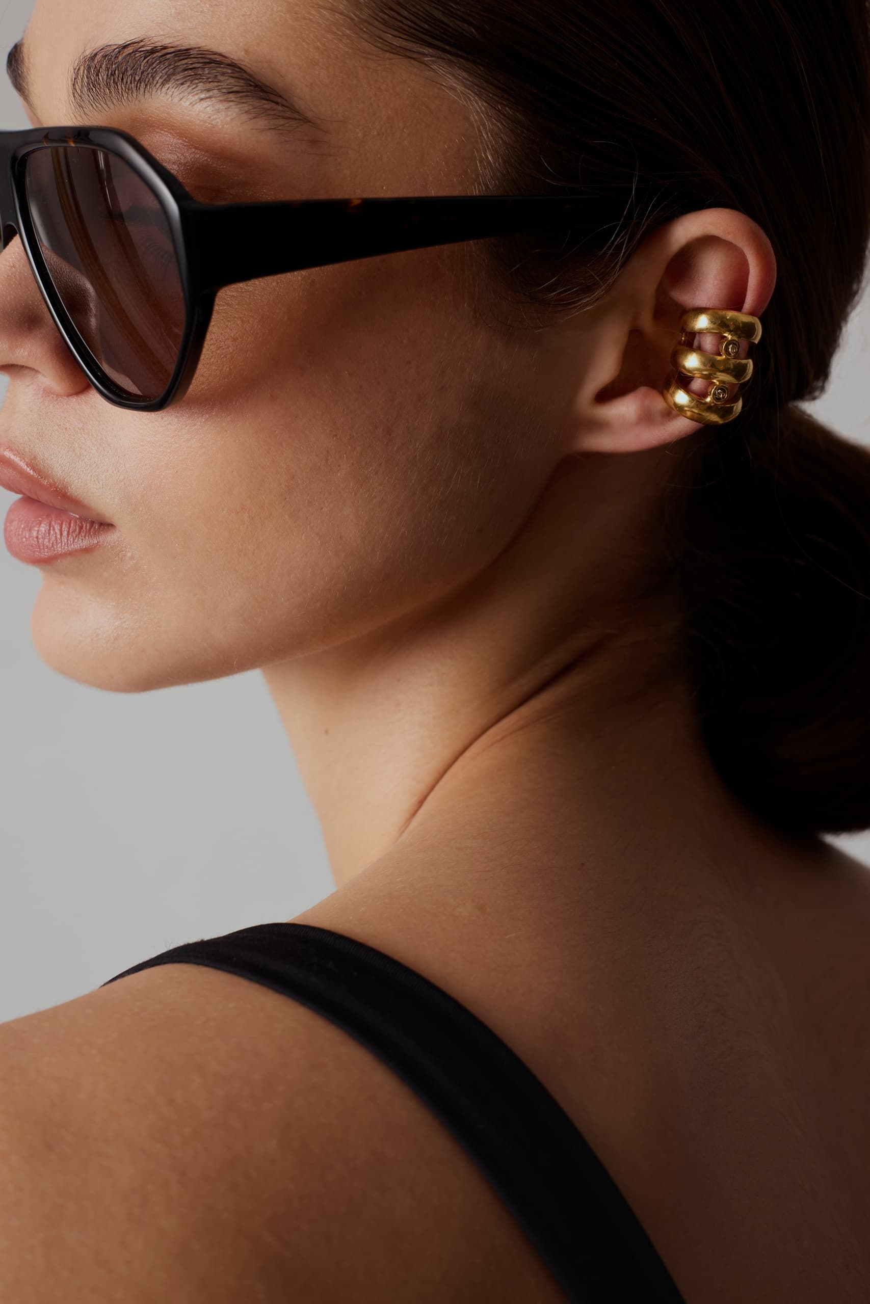 Woman in sunglasses wearing gold ear cuff.