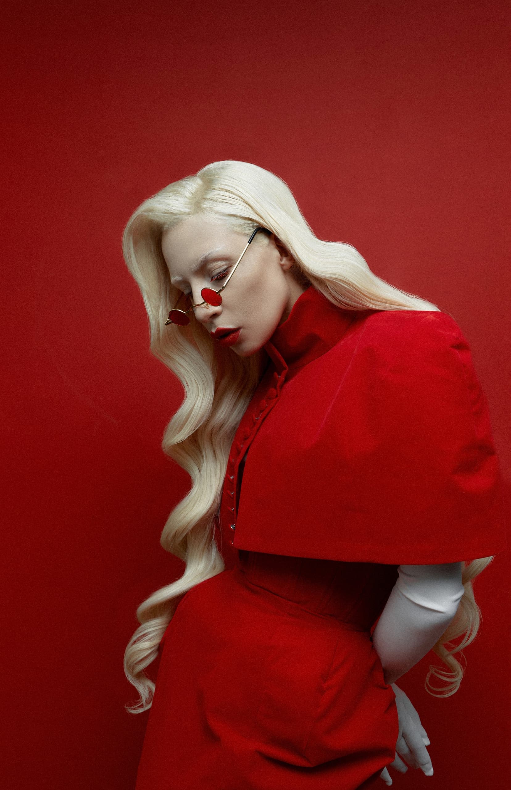 Model in vibrant red outfit and sunglasses against a red background.