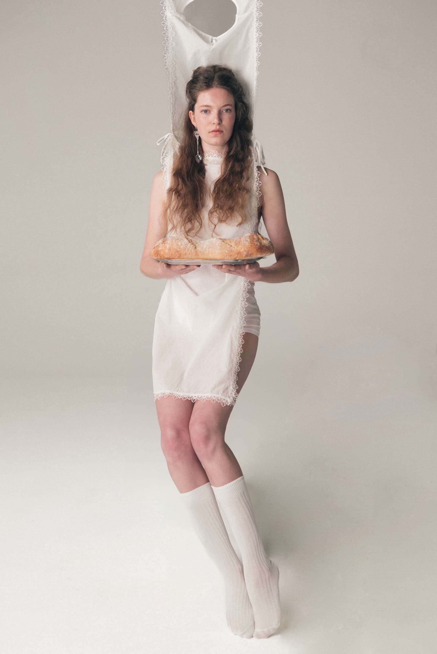 Woman in unique white dress holds a bread loaf on a tray.