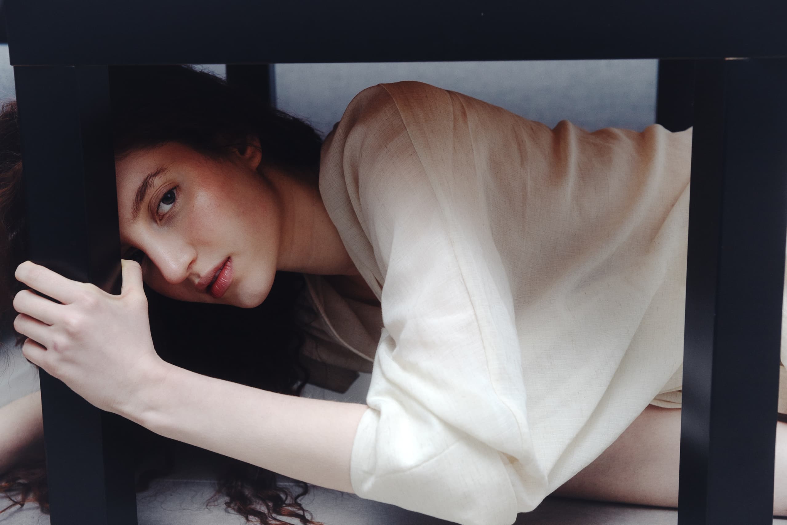 Woman crouching beneath a table in a beige dress.