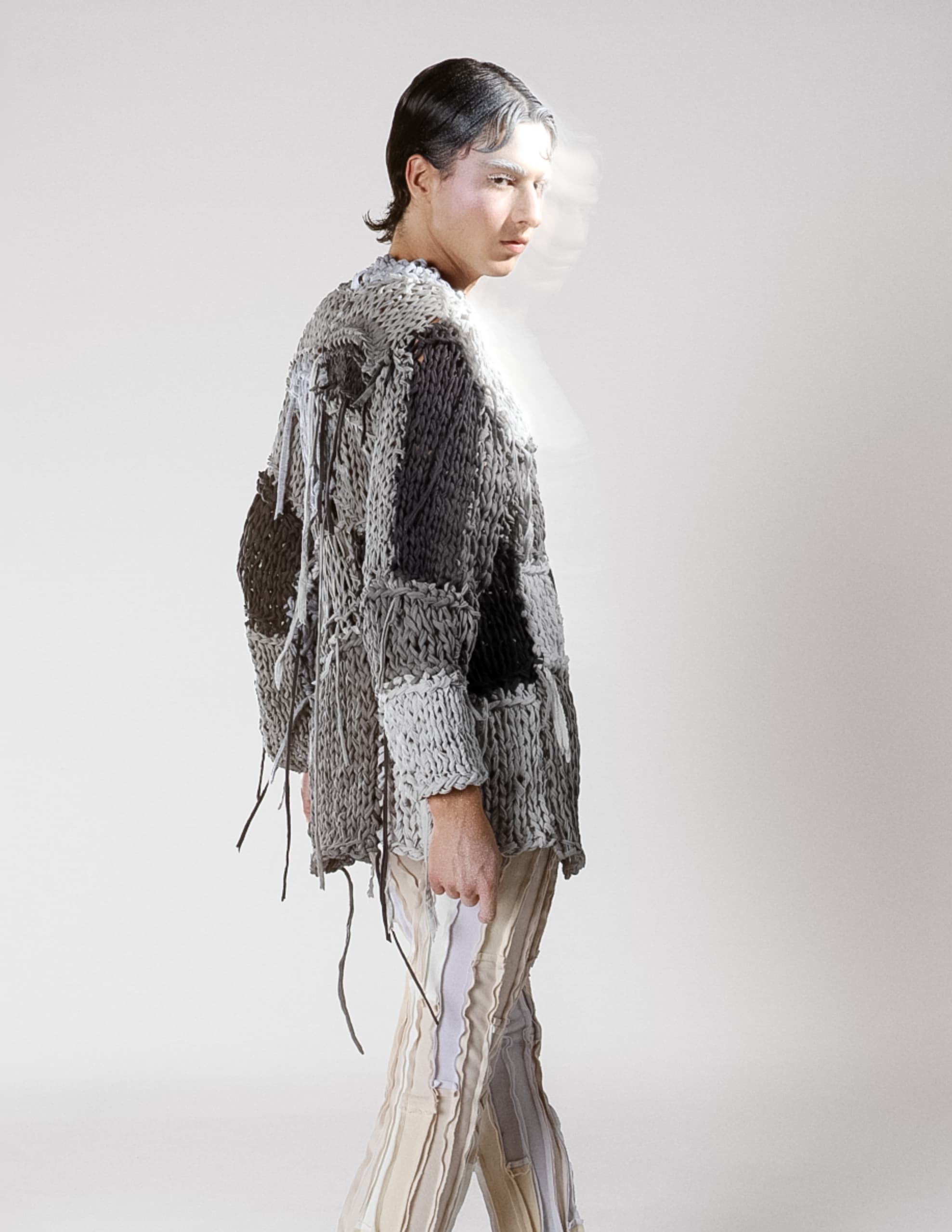 Person in textured knitwear and striped pants, minimal background.