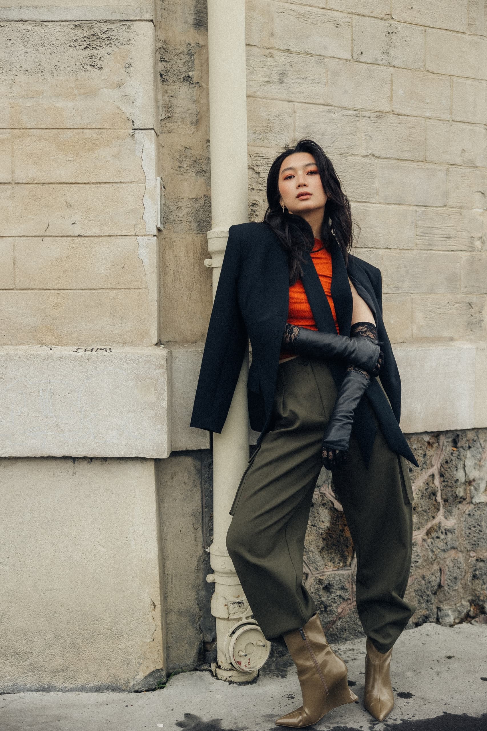 Fashionable woman in stylish attire posing against a textured wall.