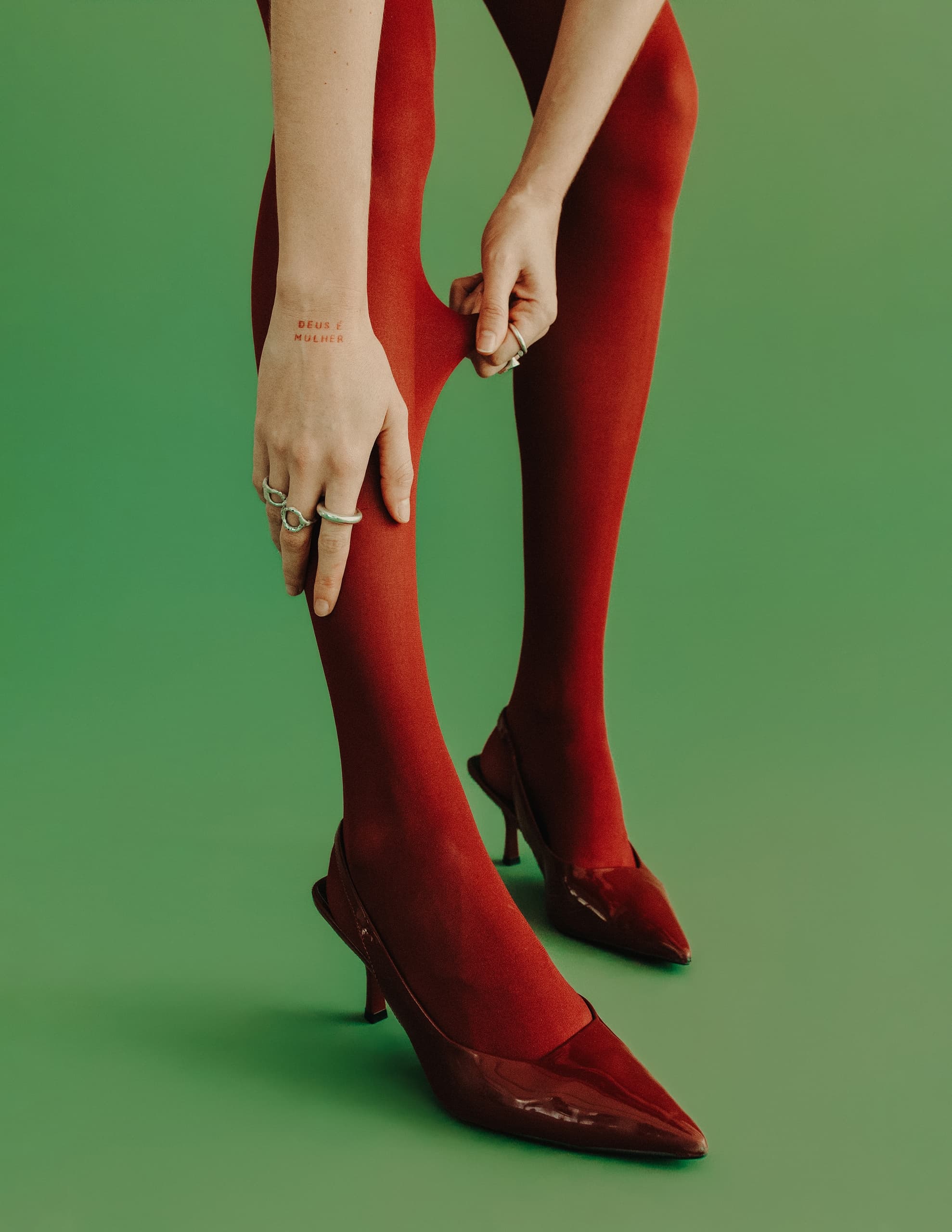 Woman adjusting red tights and heels on green background.