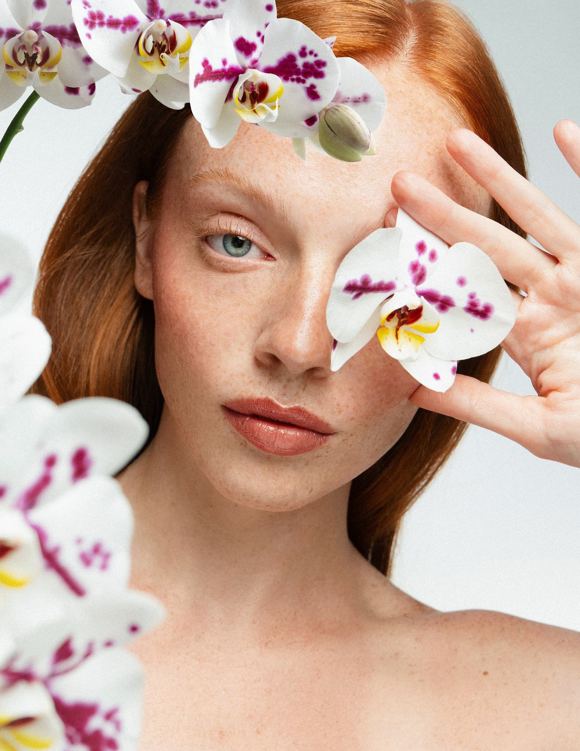 Woman with orchids covering eye, showcasing beauty and nature harmony.