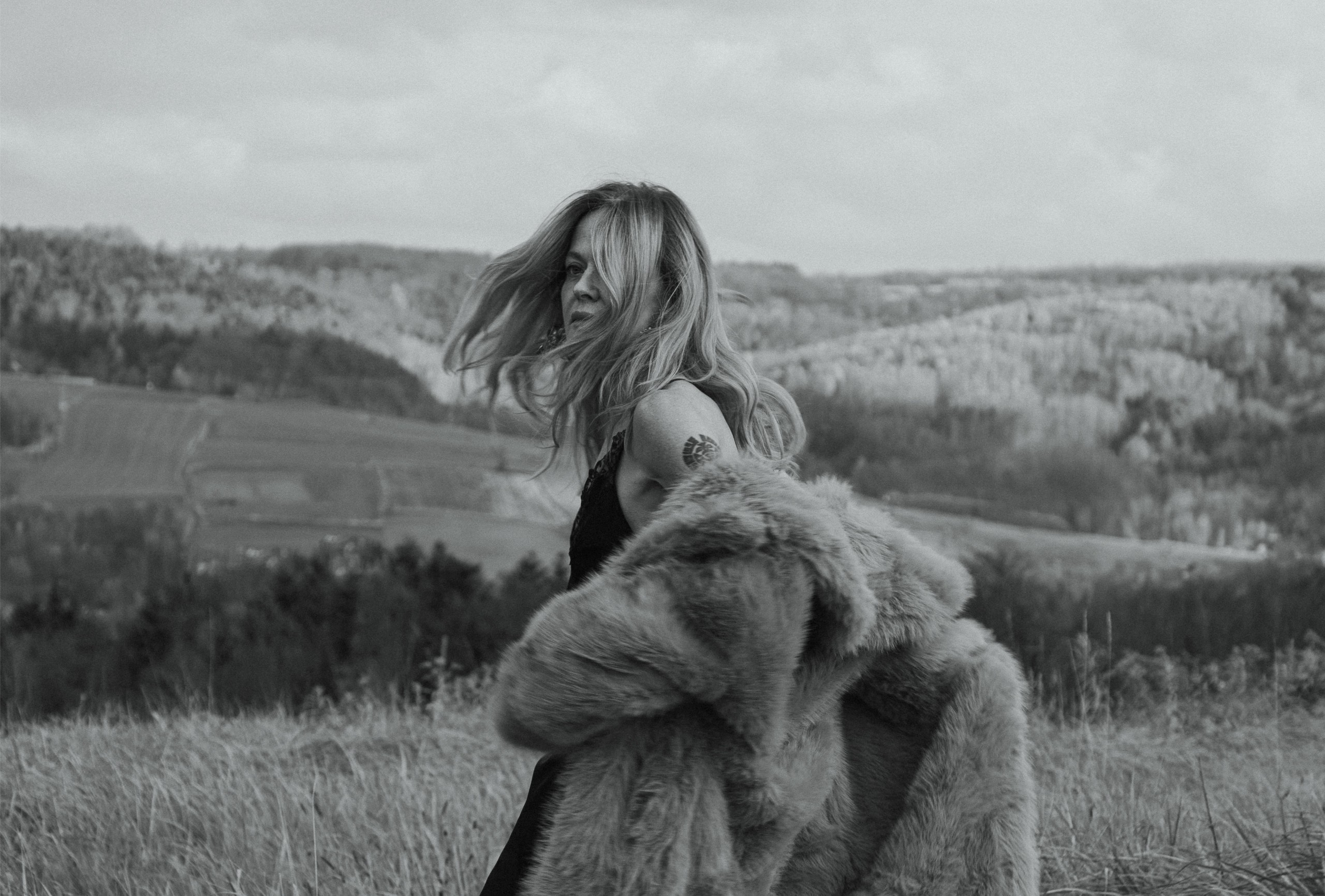 Woman with fur coat in windy outdoor field, black and white photography.