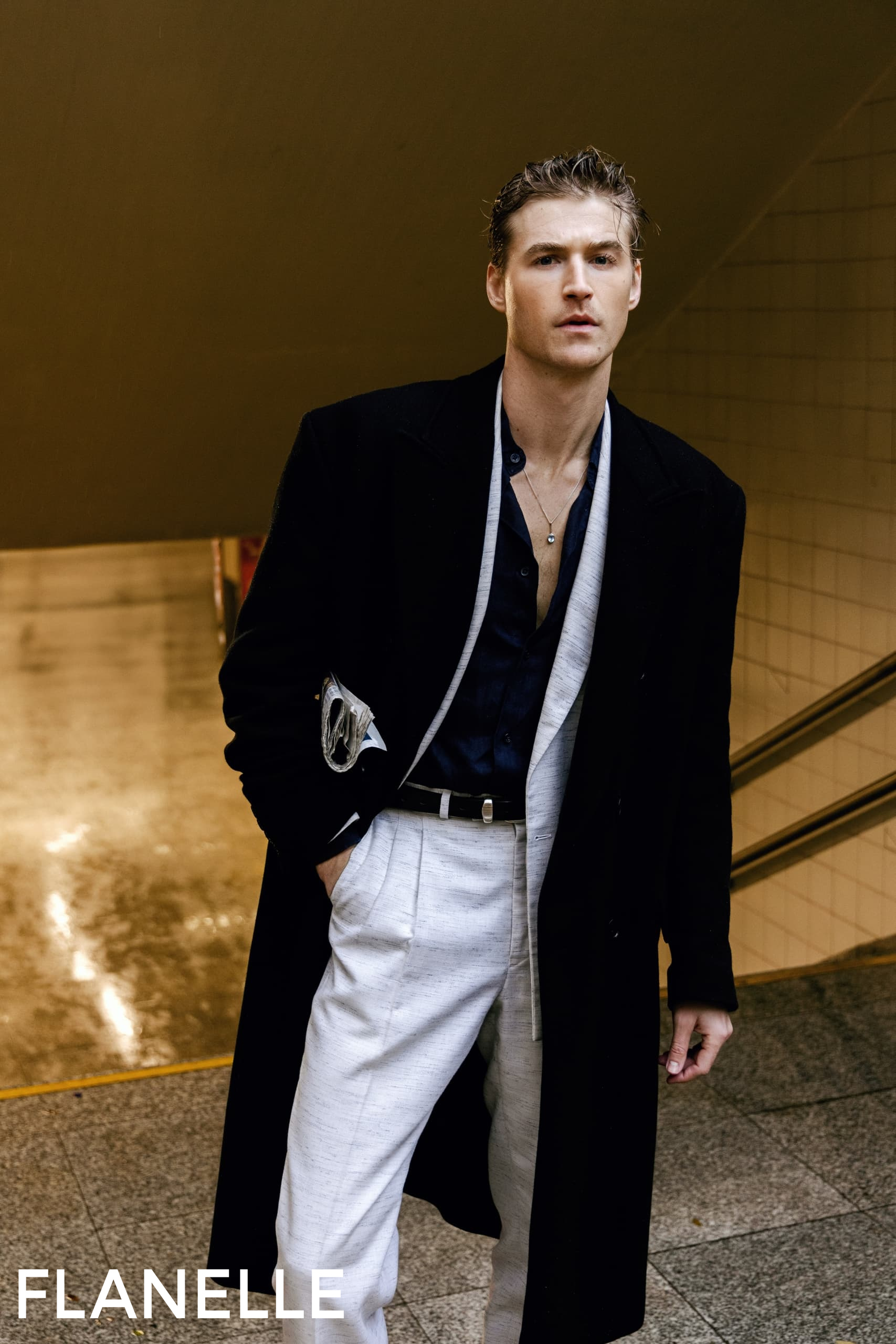 Stylish man in black coat and white pants on urban stairs. Fashionable look.