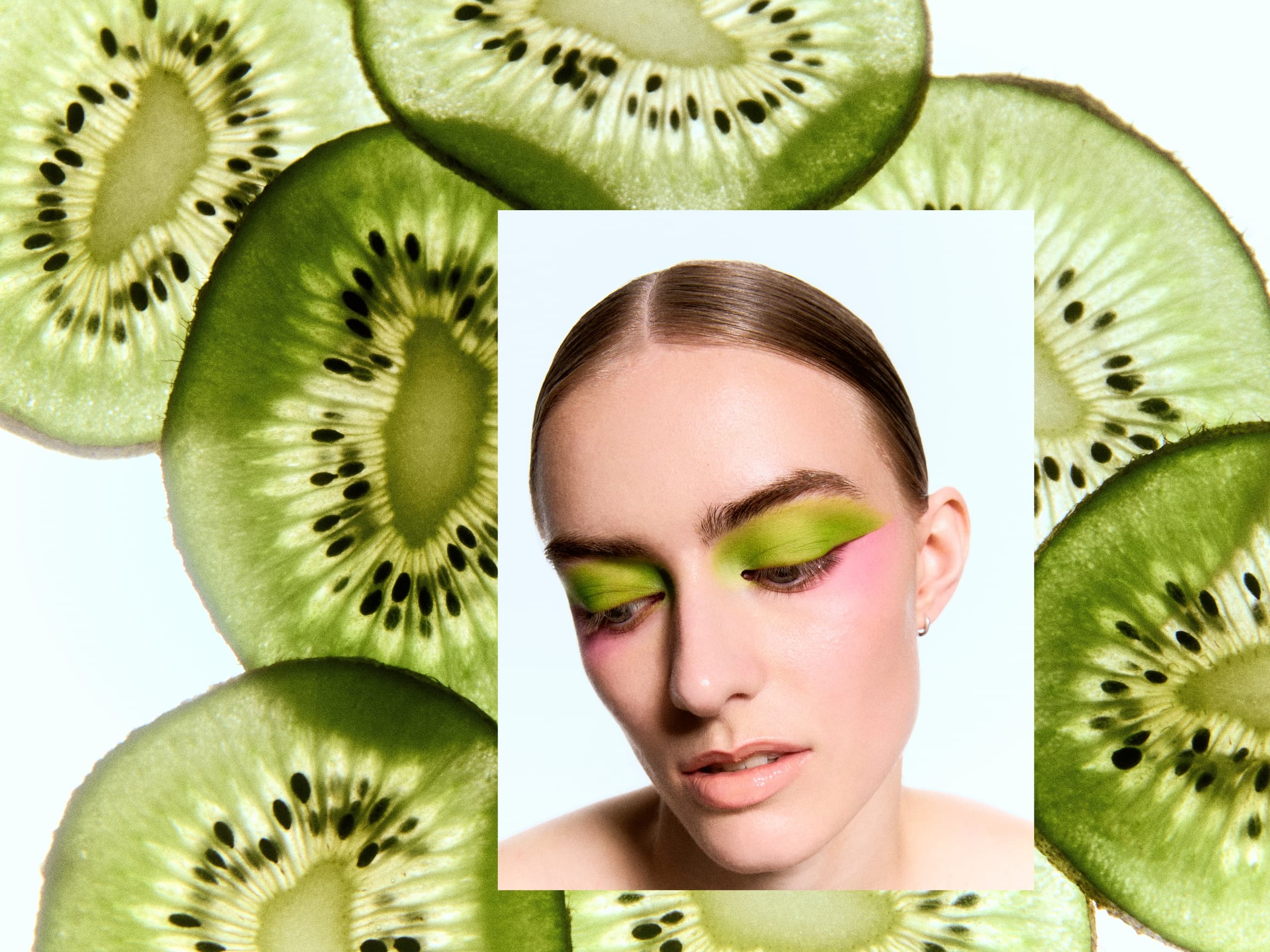 Model with green eyeshadow, surrounded by sliced kiwi fruit for vibrant contrast.