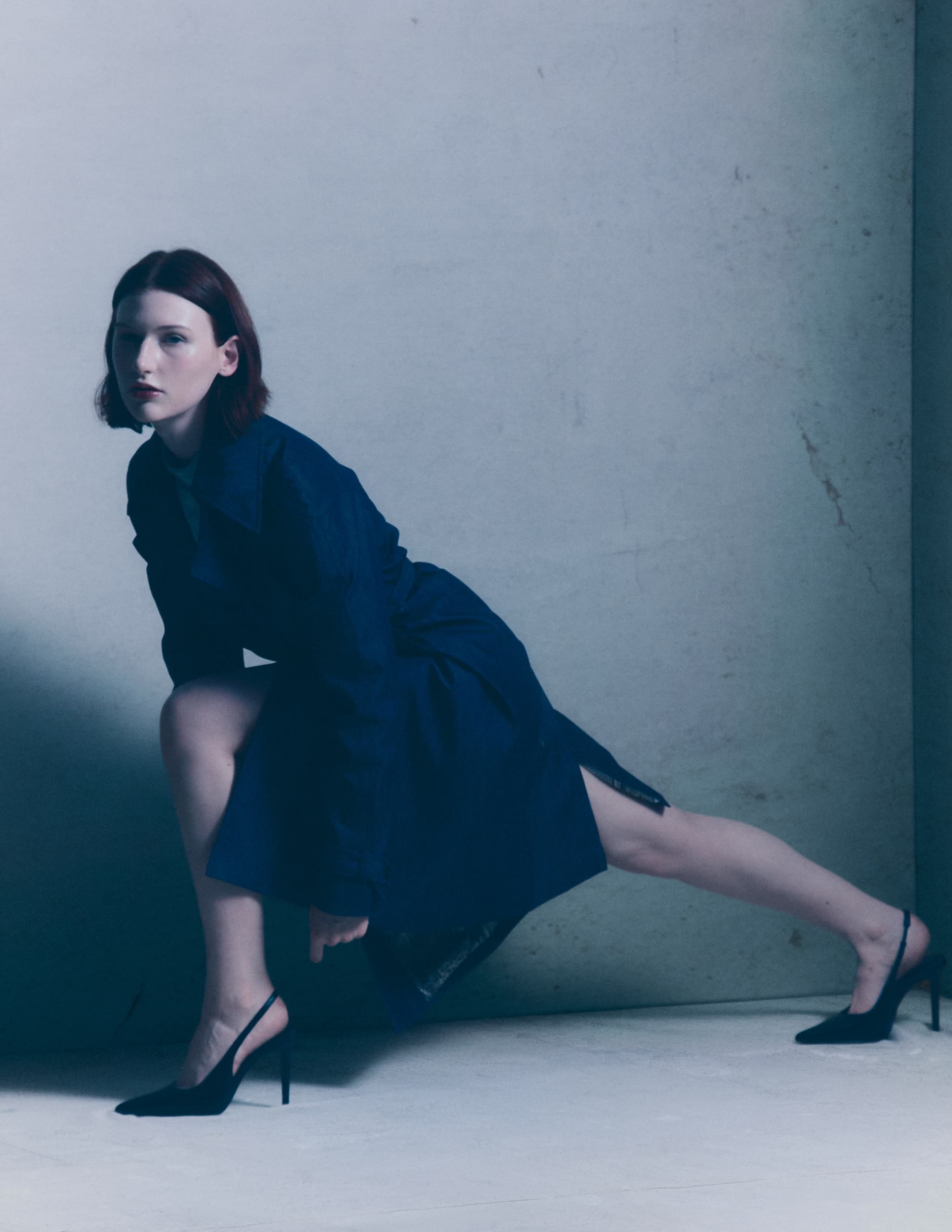 Woman in a blue coat posing stylishly against a minimalistic background.