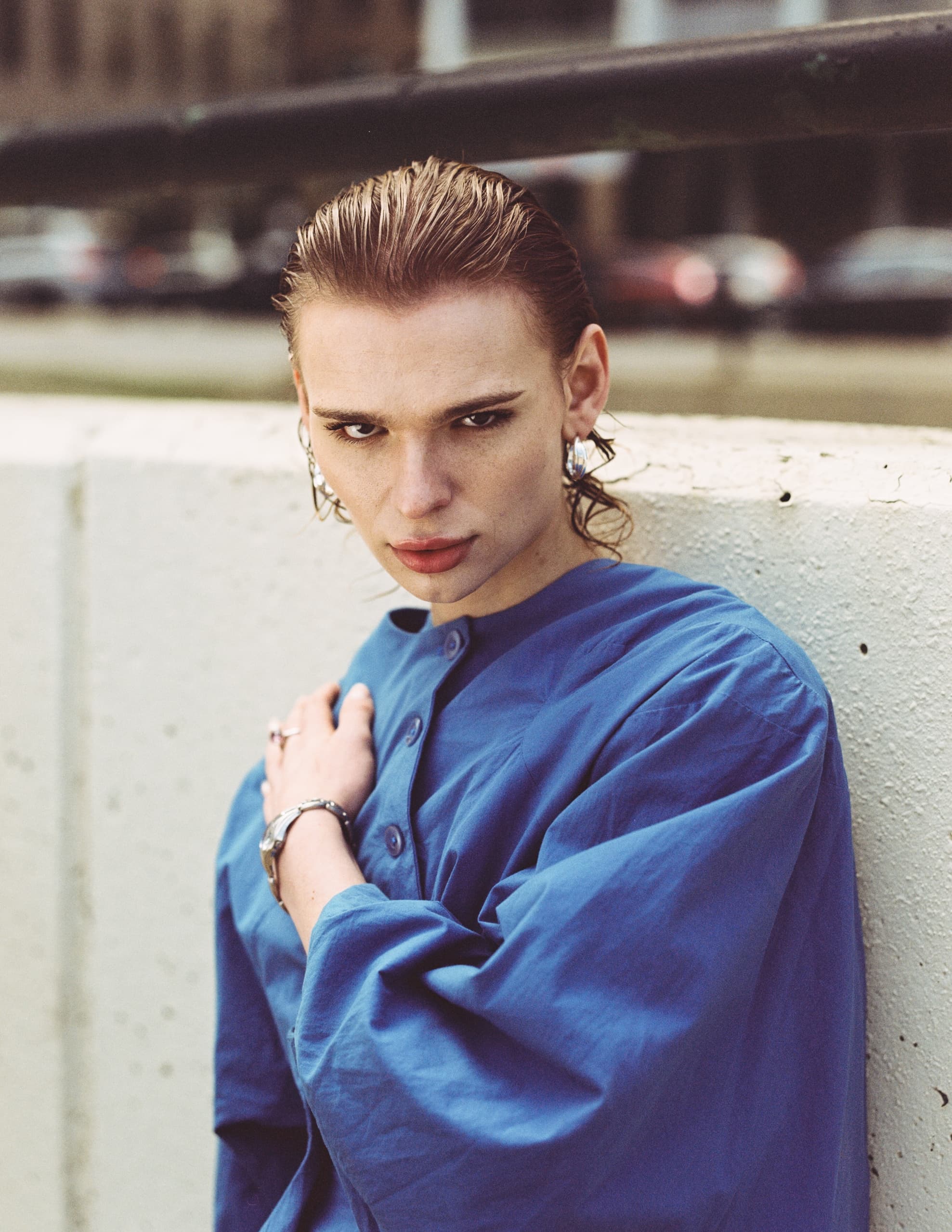 Person in blue shirt with wet hair, leaning on a concrete wall, looking serious.
