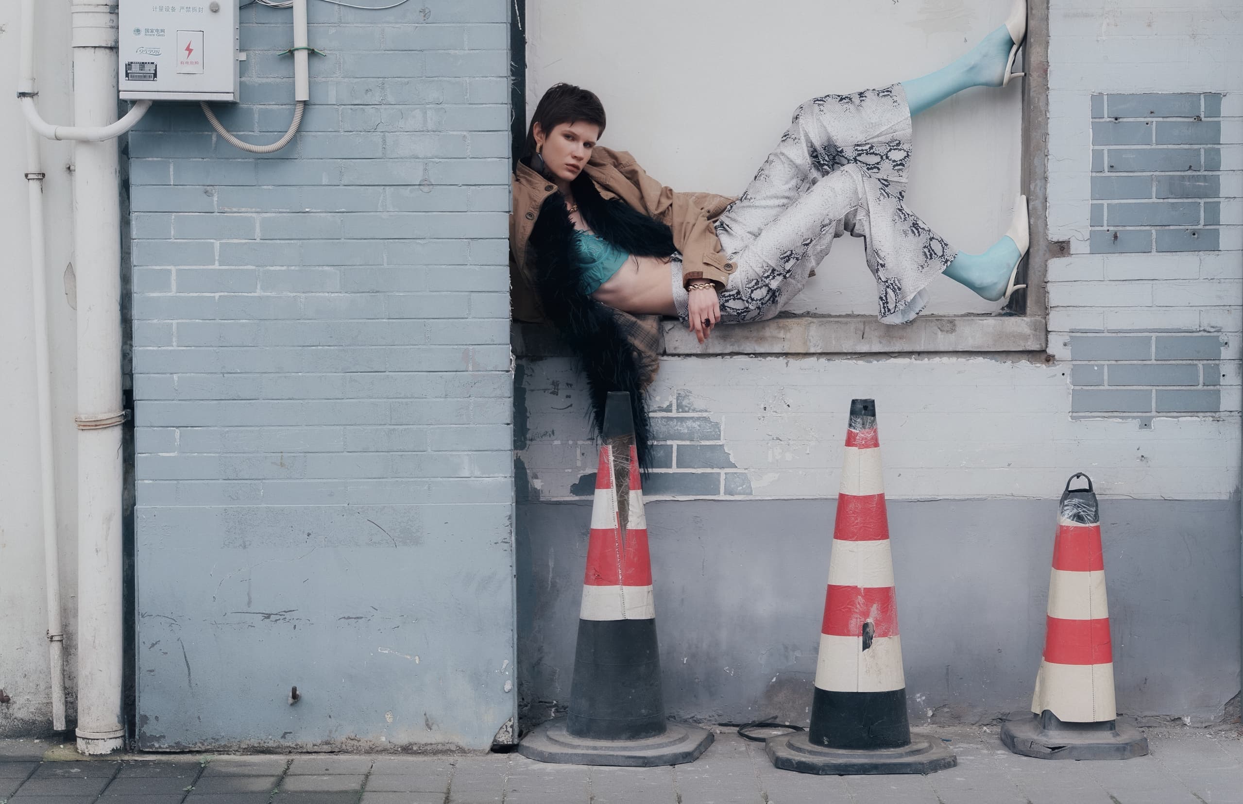Fashionable person posing creatively by a brick wall with traffic cones.
