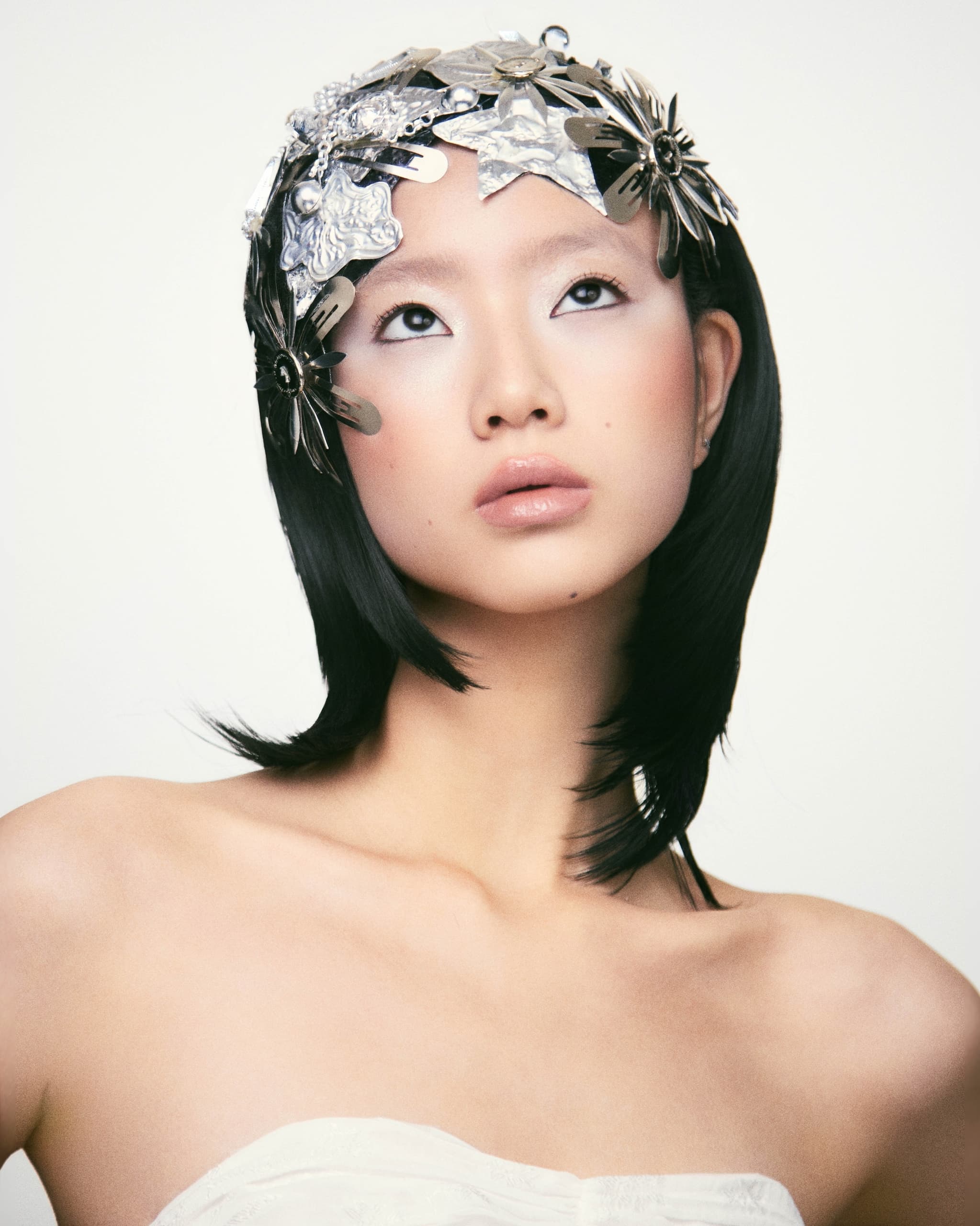 Woman with black hair wearing a silver floral headpiece, looking upwards.