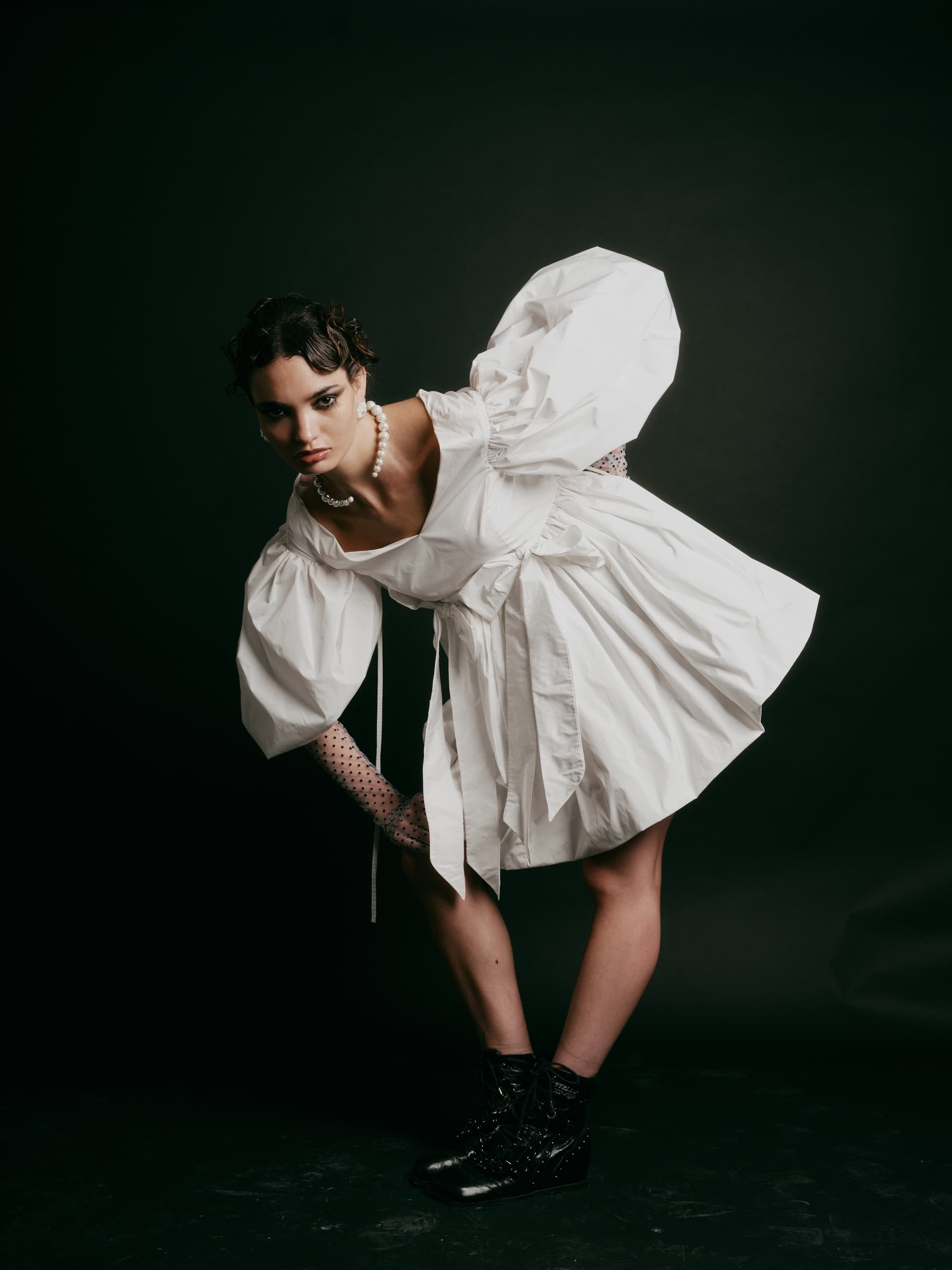 Fashion model in white dress poses with dramatic flair against dark background.