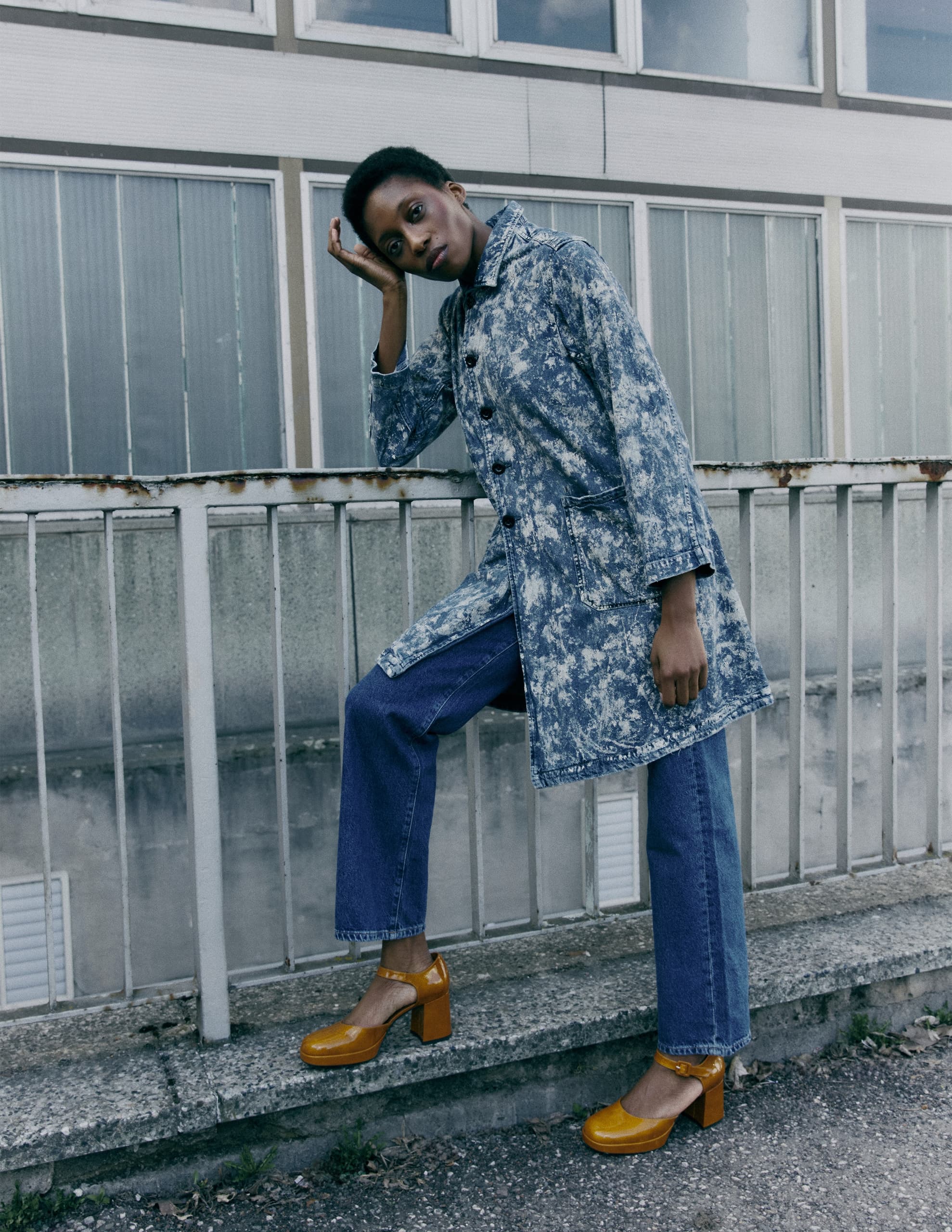 Person in denim outfit with yellow heels poses by modern building.