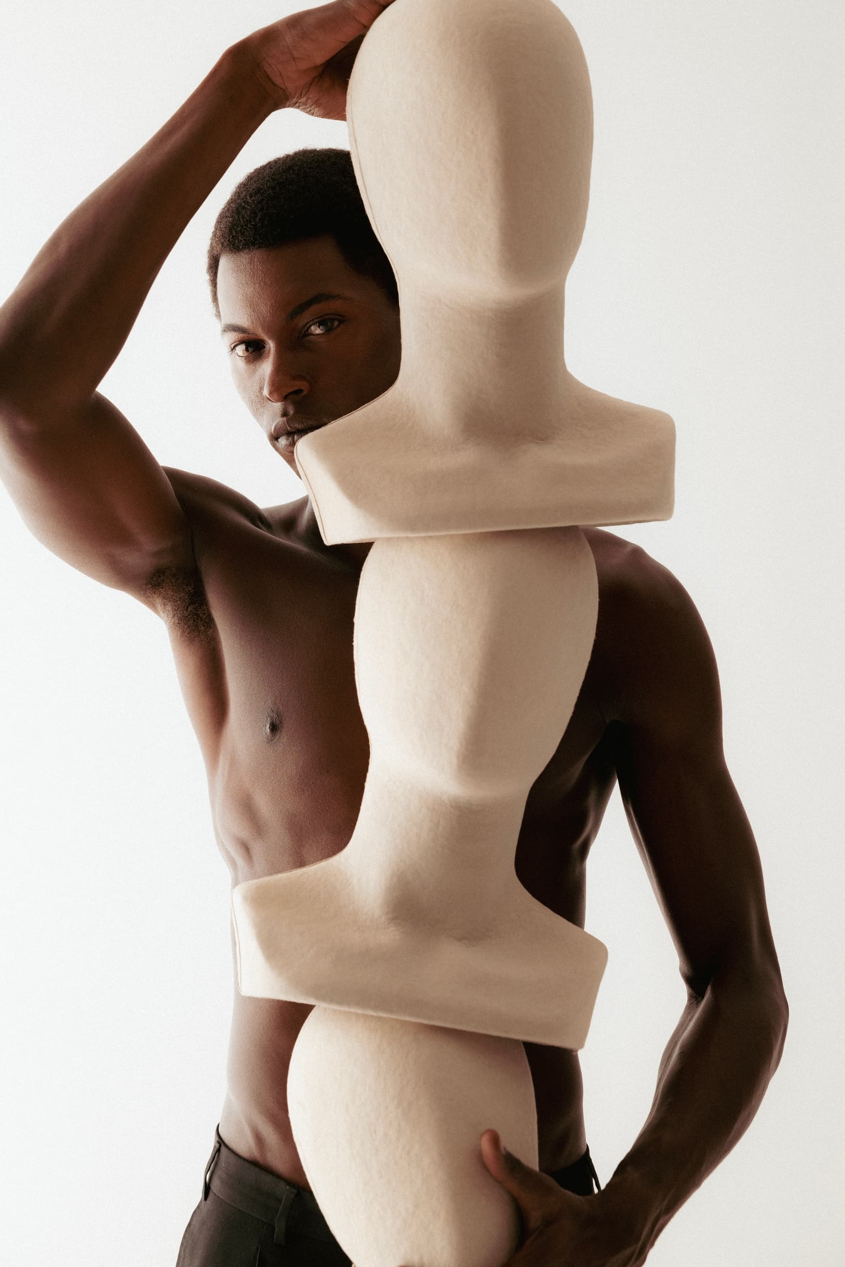 Man posing with abstract mannequin busts, artistic fashion photo.